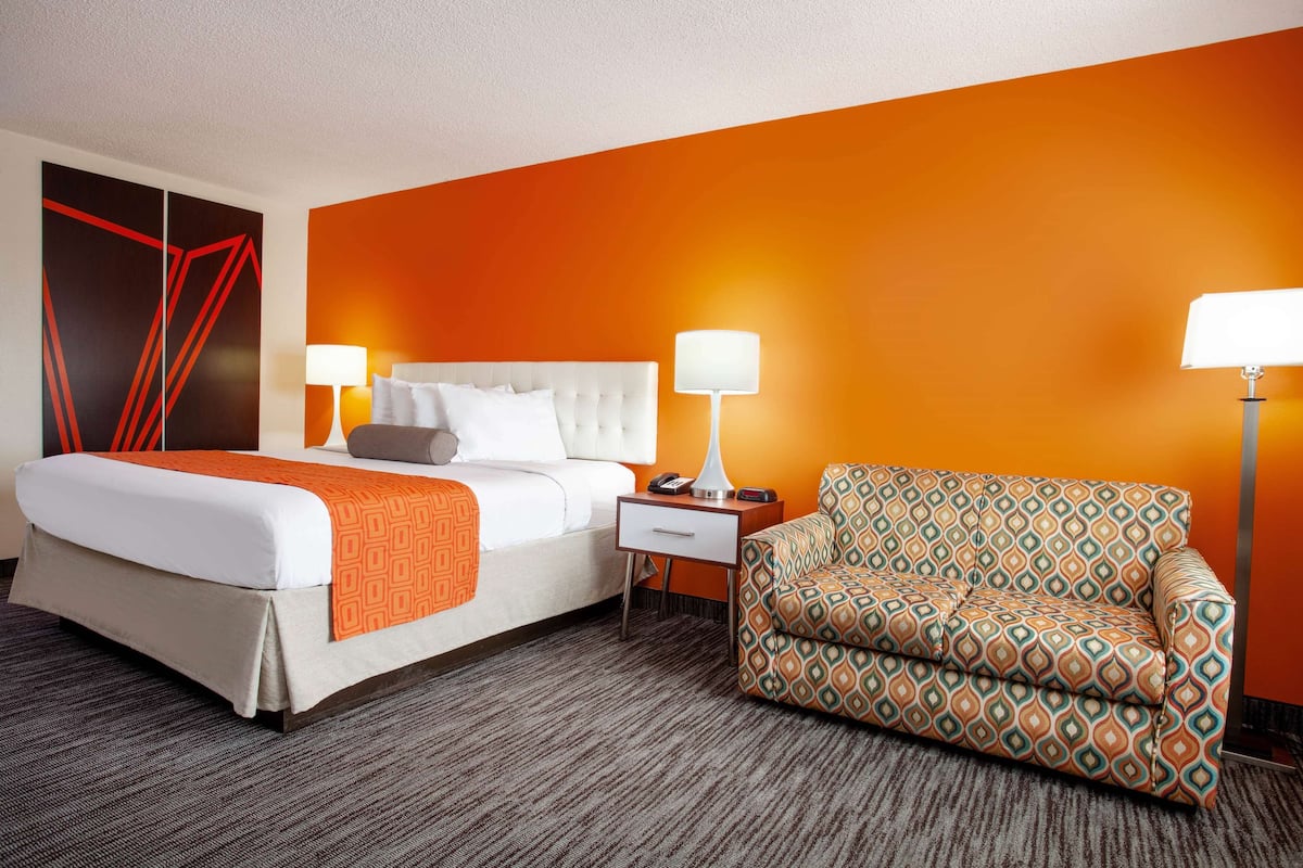 A hotel room with a bed, two bedside tables, a sofa, and a large abstract painting on the wall.