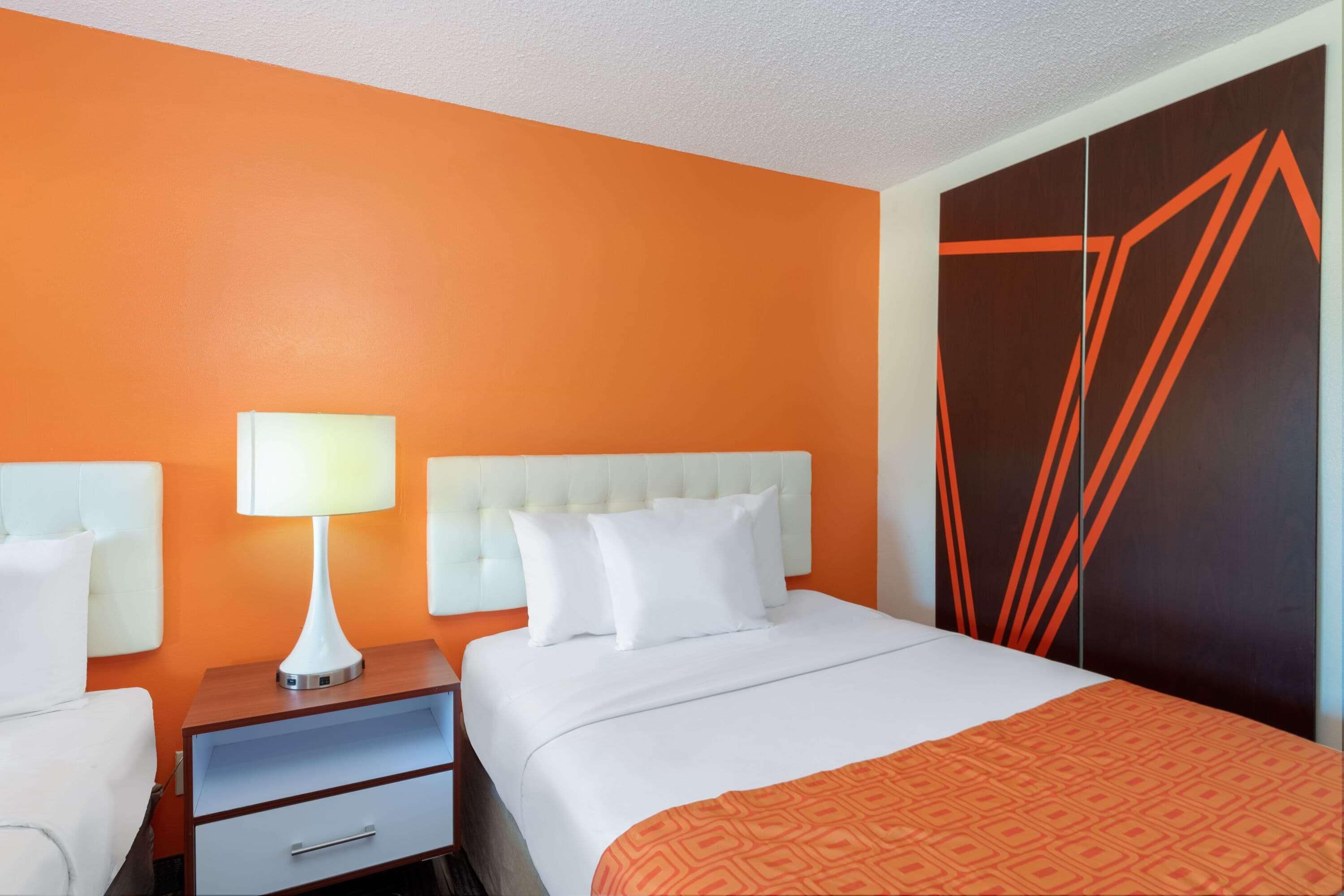A hotel room with a white bed, a nightstand with a lamp, and a wardrobe with geometric patterns.