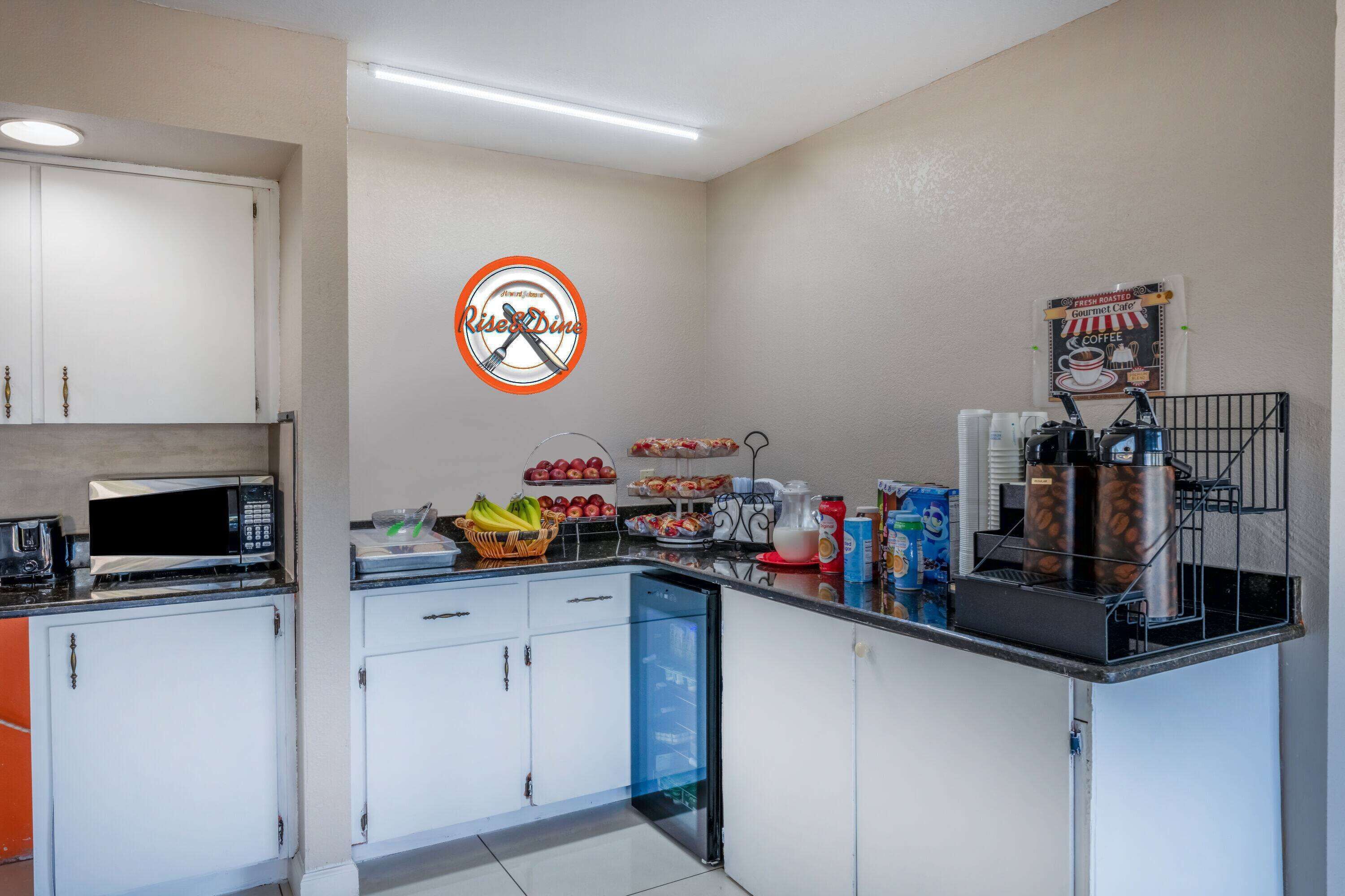 A kitchenette with a microwave, sink, and cabinets. There are fruits and a coffee station on the counter.