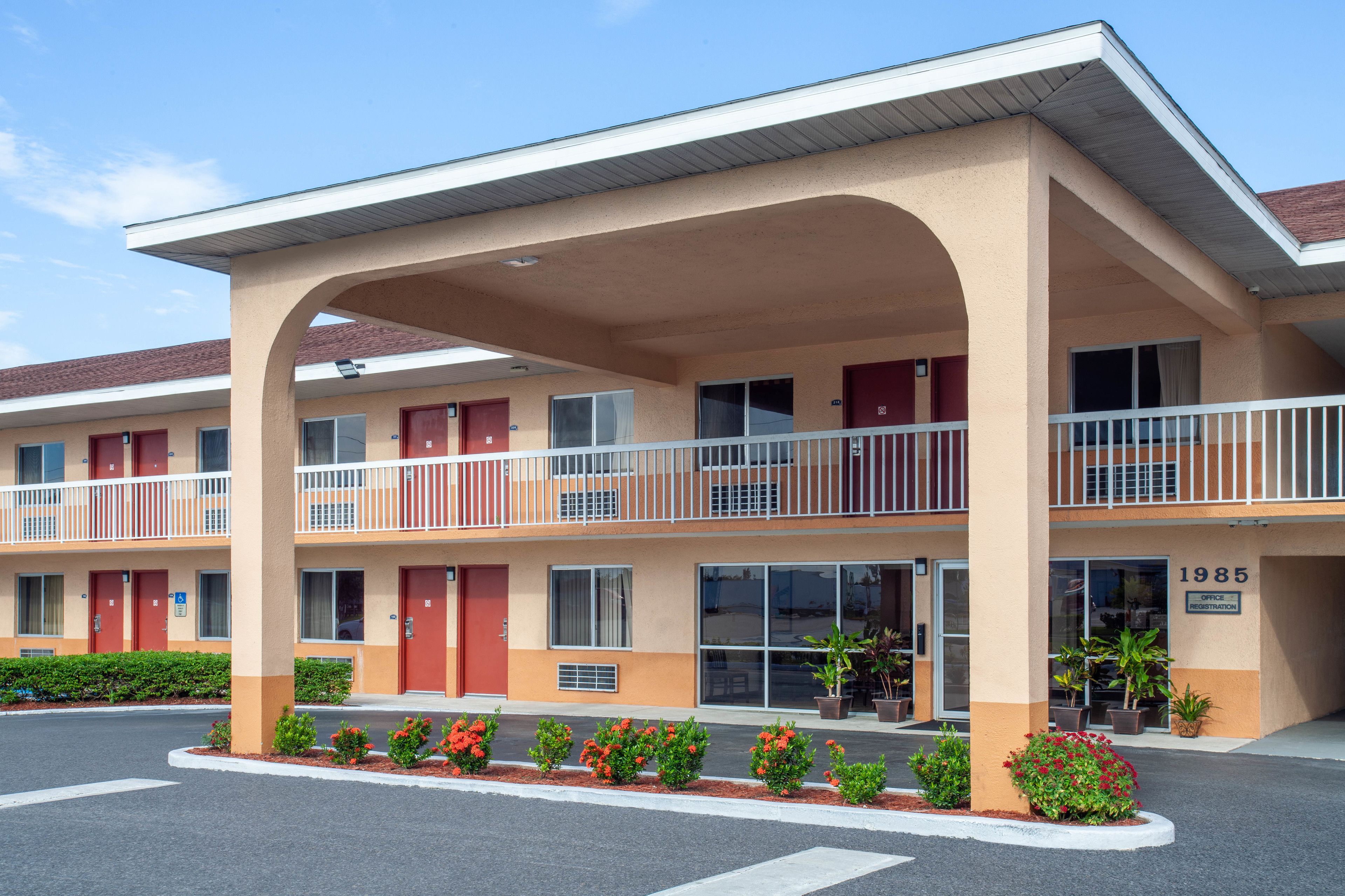 Un motel à plusieurs étages, avec une façade beige, des portes rouges et des balcons.