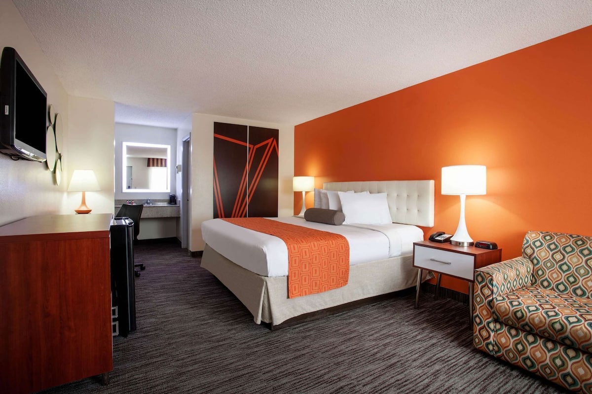 A hotel room with a bed, bedside tables, a desk, a chair, and a television.