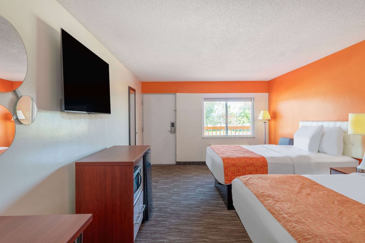 A hotel room with two beds, a TV, a desk, and a window.