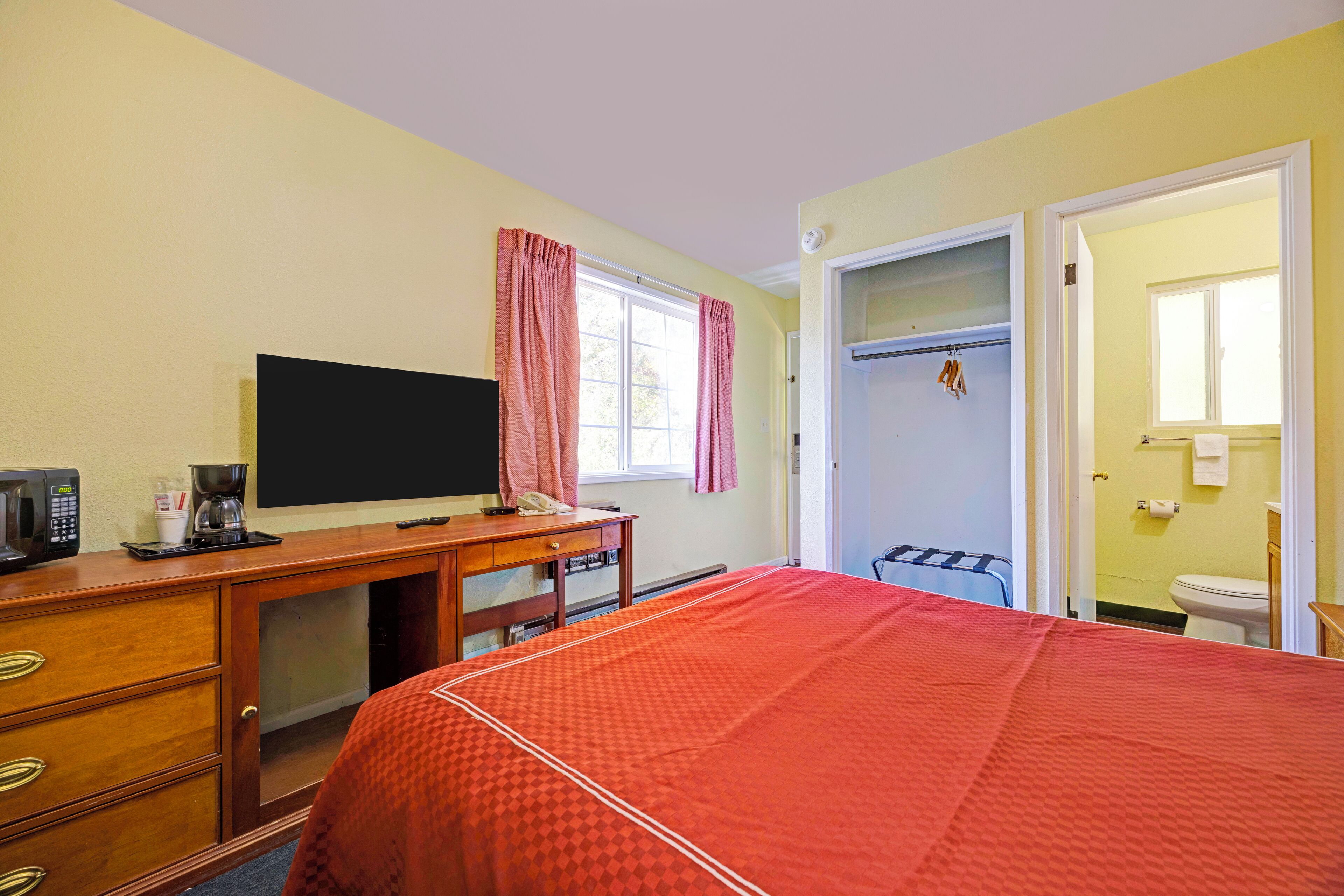 Een hotelkamer met een bed, een bureau met een televisie, een magnetron en een koffiezetapparaat.