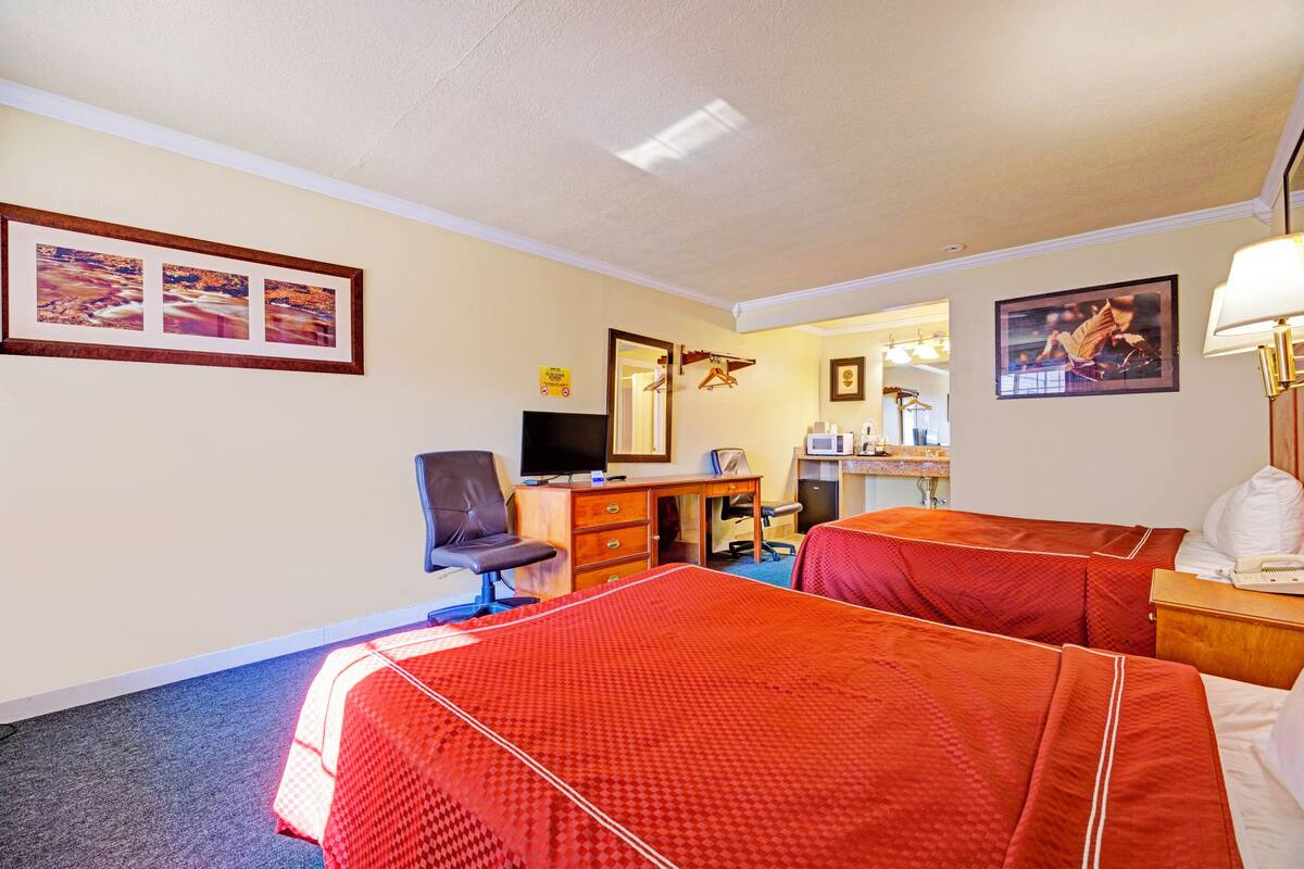 A hotel room with two beds, a desk, a chair, a television, and a bathroom visible through an open door.