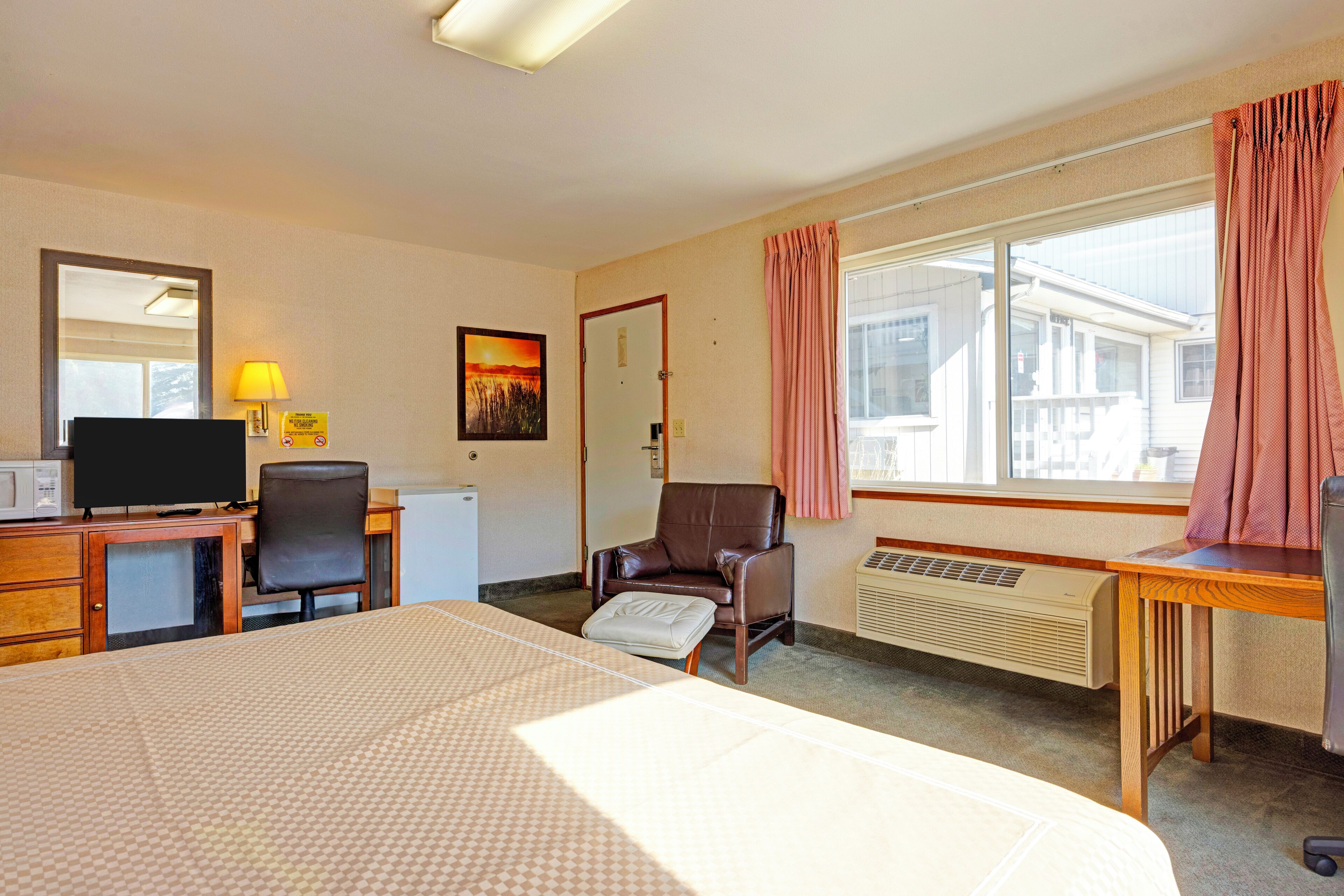 Habitación de hotel con cama, escritorio, silla, televisor y ventana con cortinas.