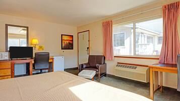 Habitación de hotel con cama, escritorio, silla, televisor y ventana con cortinas.