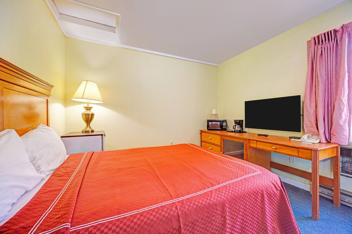 A hotel room with a bed, a desk with a television, a lamp, and a telephone.