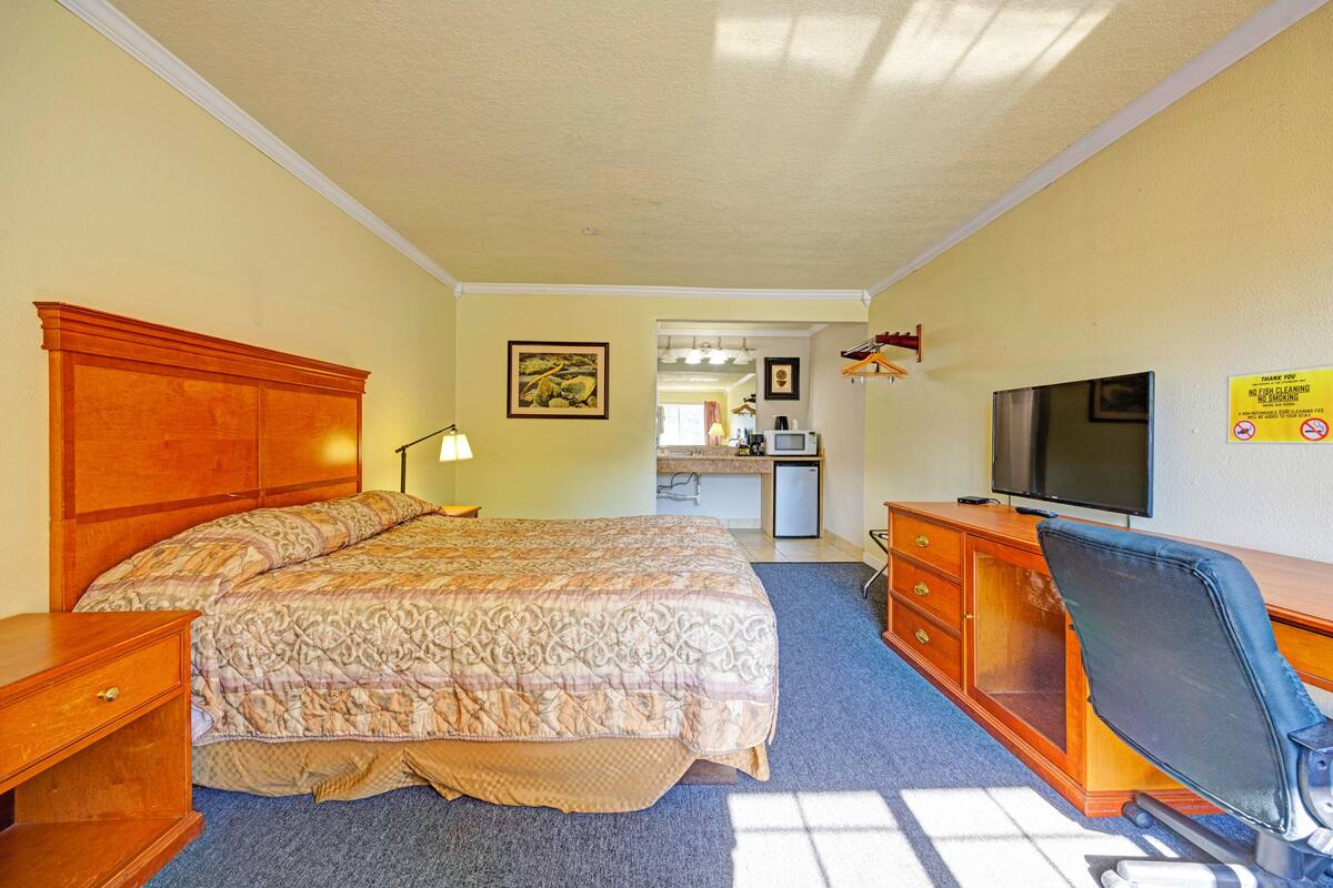 A hotel room with a large bed, a desk with a chair, a television, and a desk lamp.