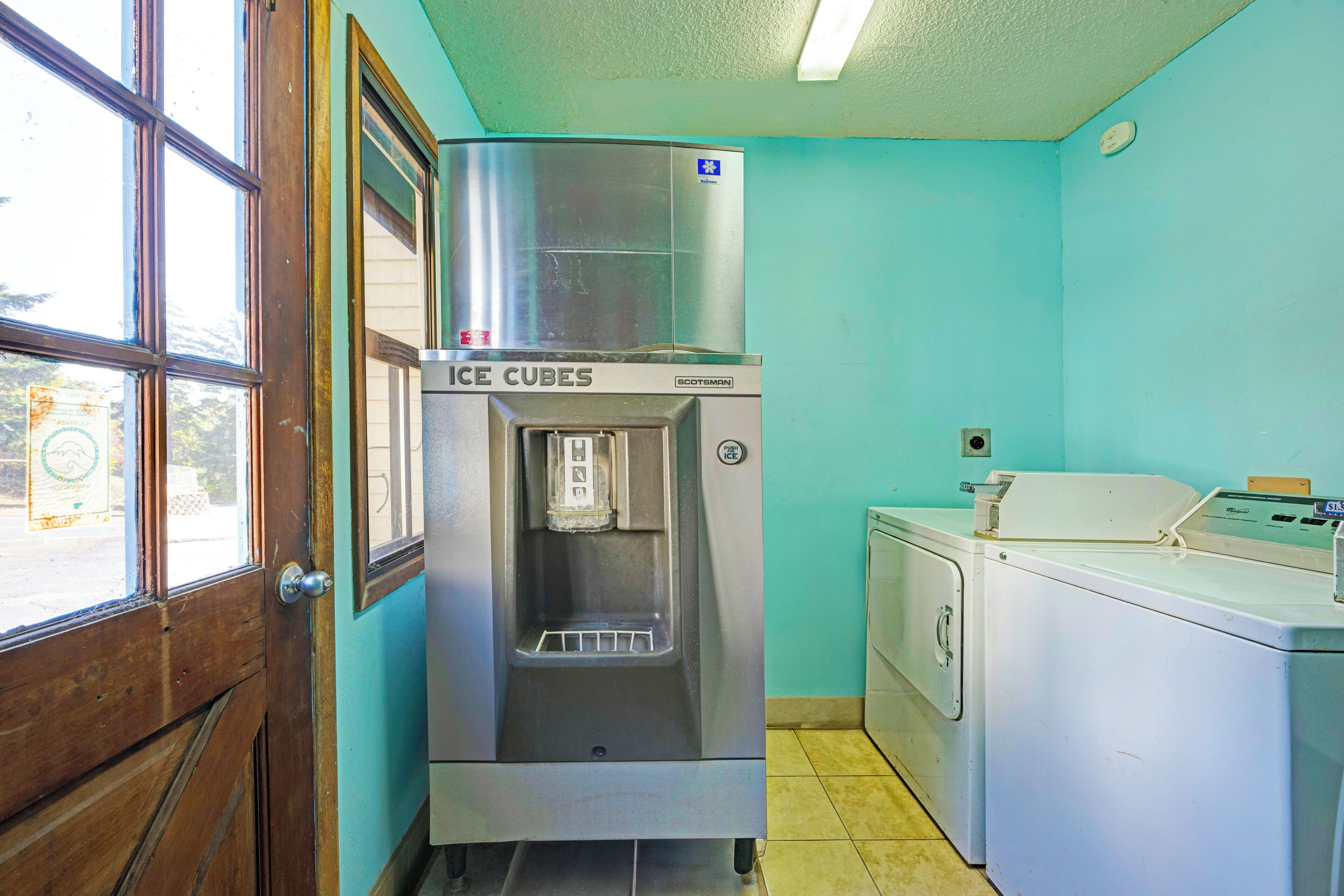 A kitchen with a stainless steel ice cube dispenser, a washing machine, and a wooden door.