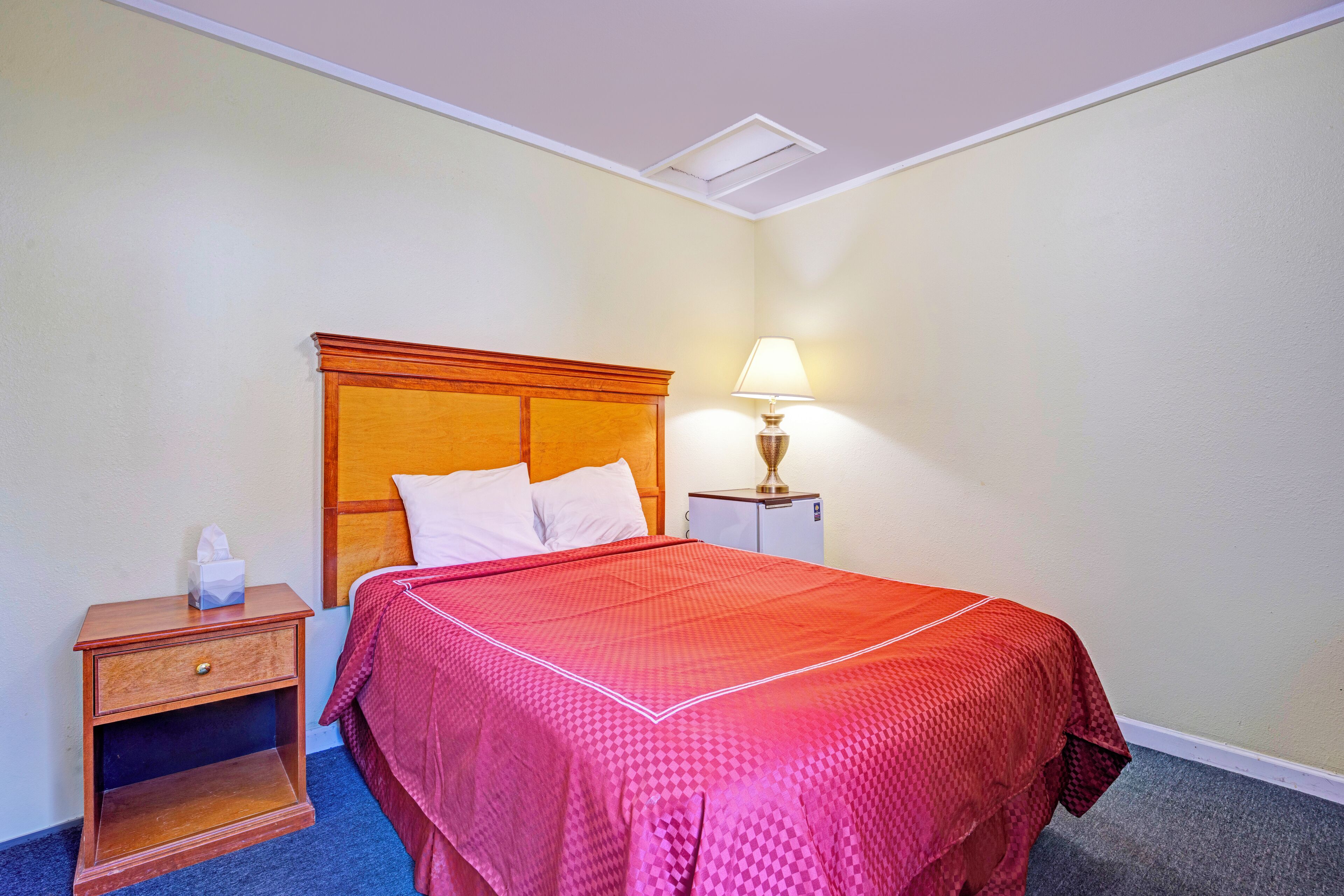 Een hotelkamer met een bed, nachtkastje, lamp en een klein kastje.