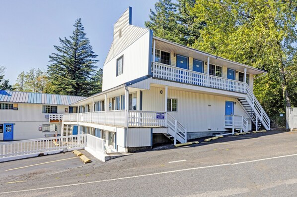 A two-story motel with a white exterior, blue doors, and a balcony on the upper floor.