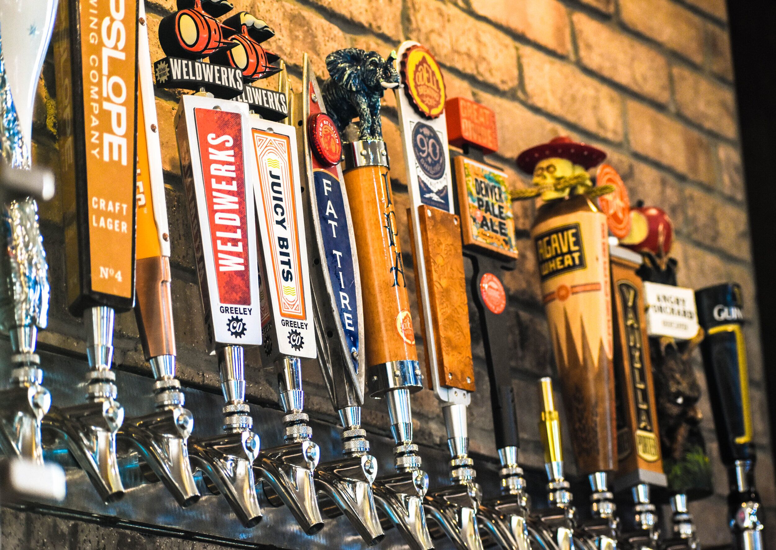 A row of beer taps with labels such as 'WELDWERKS', 'GREELEY', and 'FAT TIRE'.