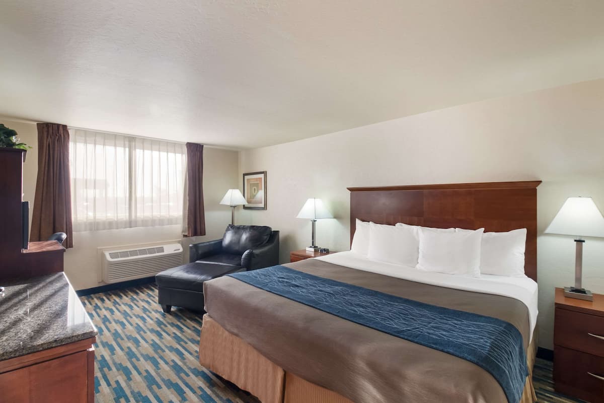 A hotel room with a large bed, a desk, a chair, and a window with curtains.