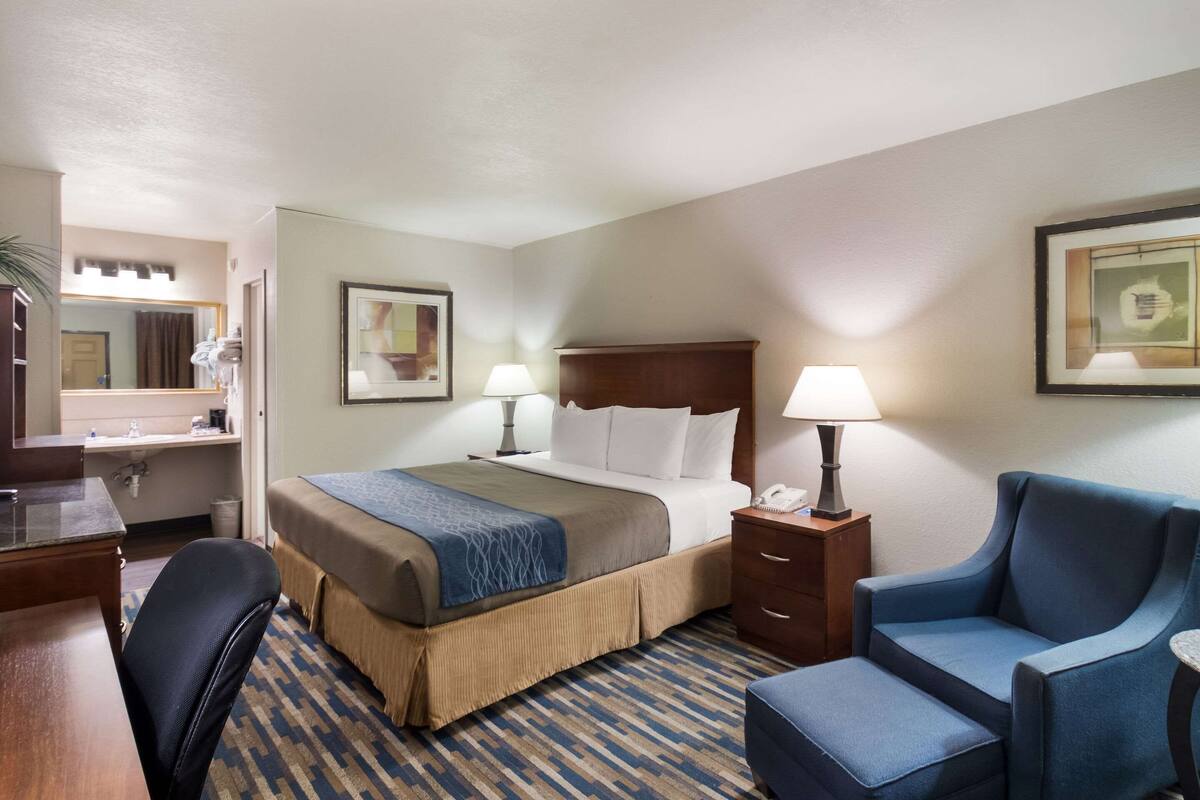 A hotel room with a bed, bedside lamps, a desk, a chair, and a mirror.