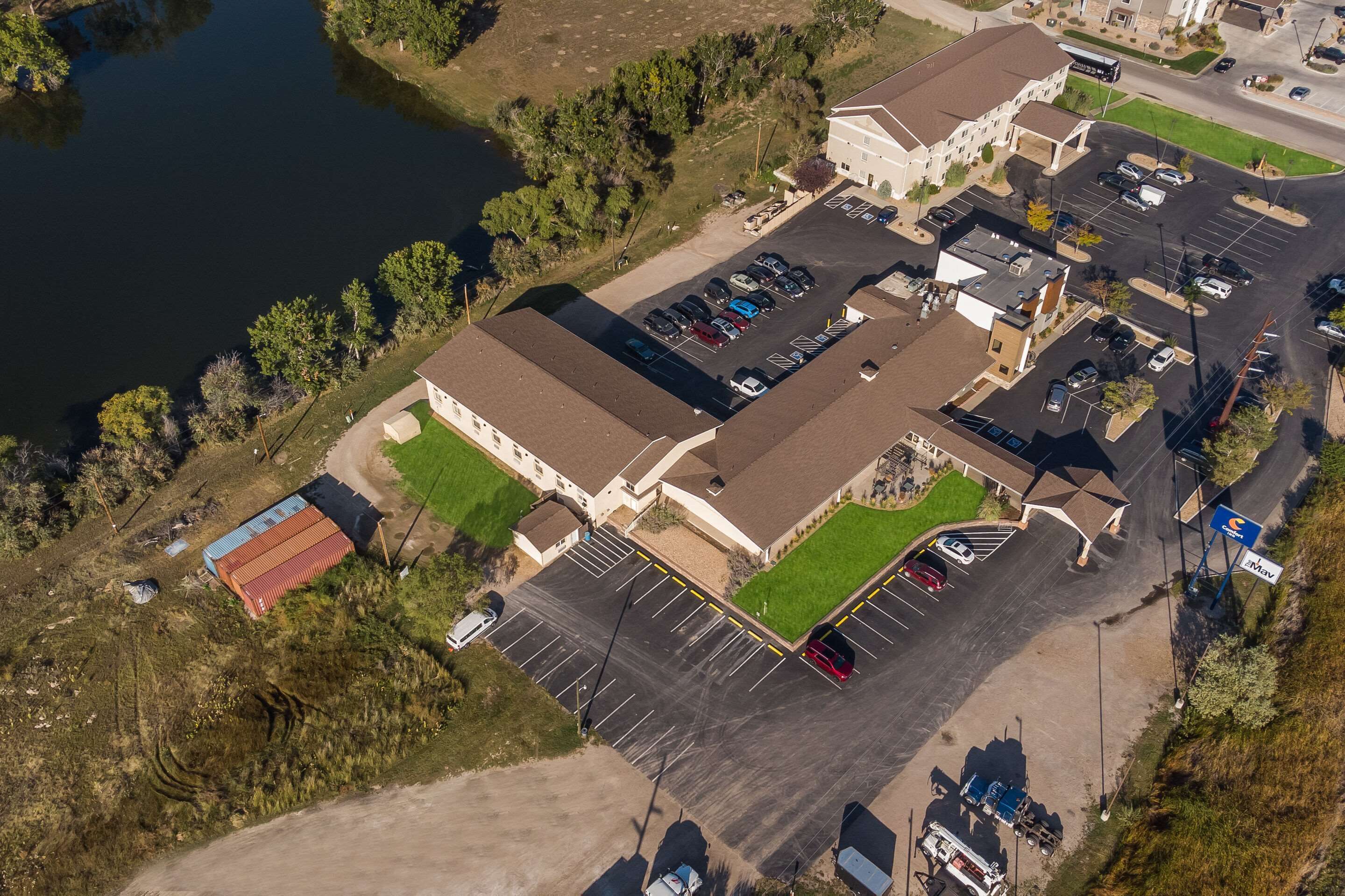 Vue aérienne d’un hôtel doté de plusieurs parkings, d’un petit lac et d’un espace verdoyant environnant.