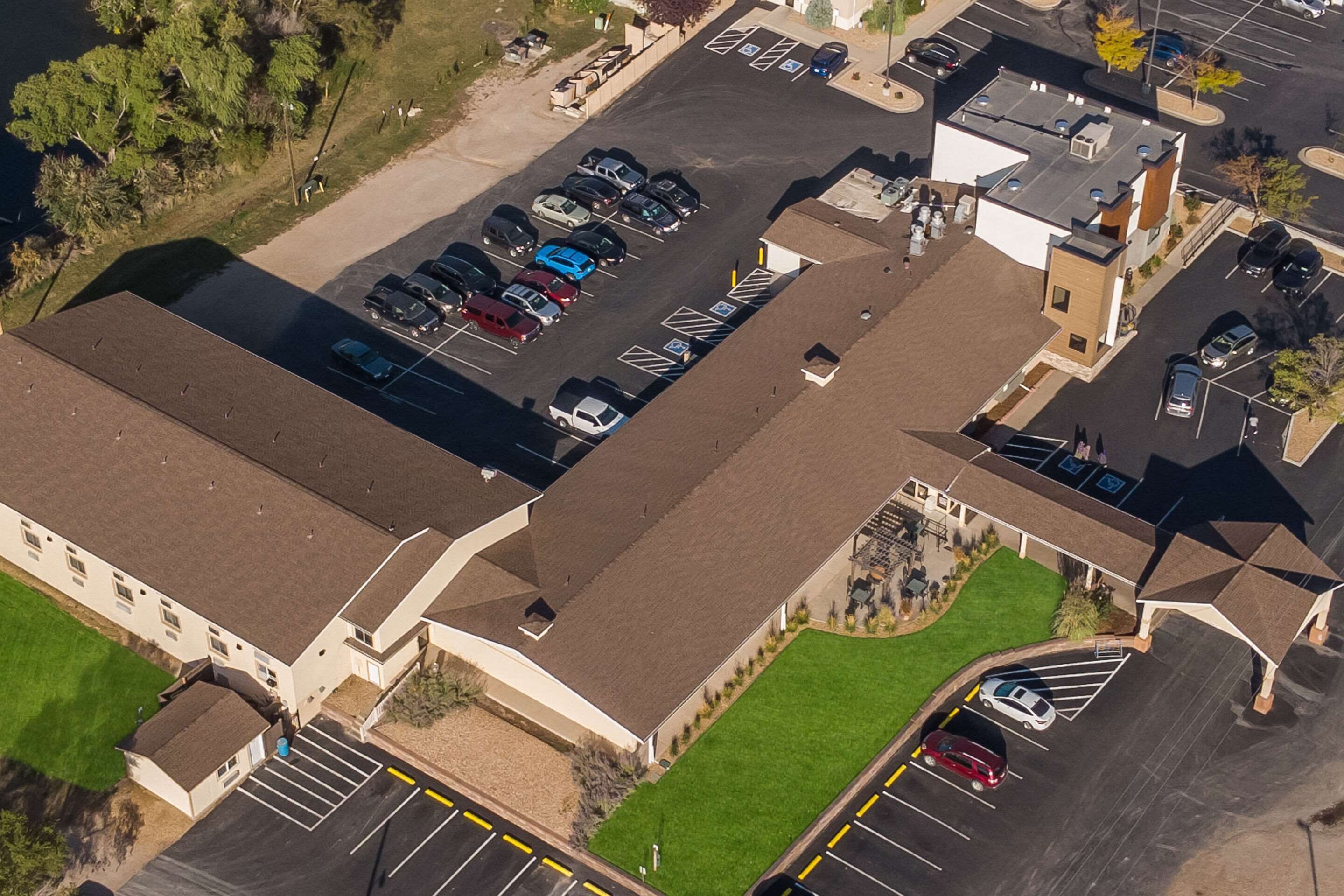 An aerial view of a parking lot with multiple cars, a building with a flat roof, and a small green area.