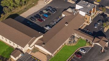 An aerial view of a parking lot with multiple cars, a building with a flat roof, and a small green area.