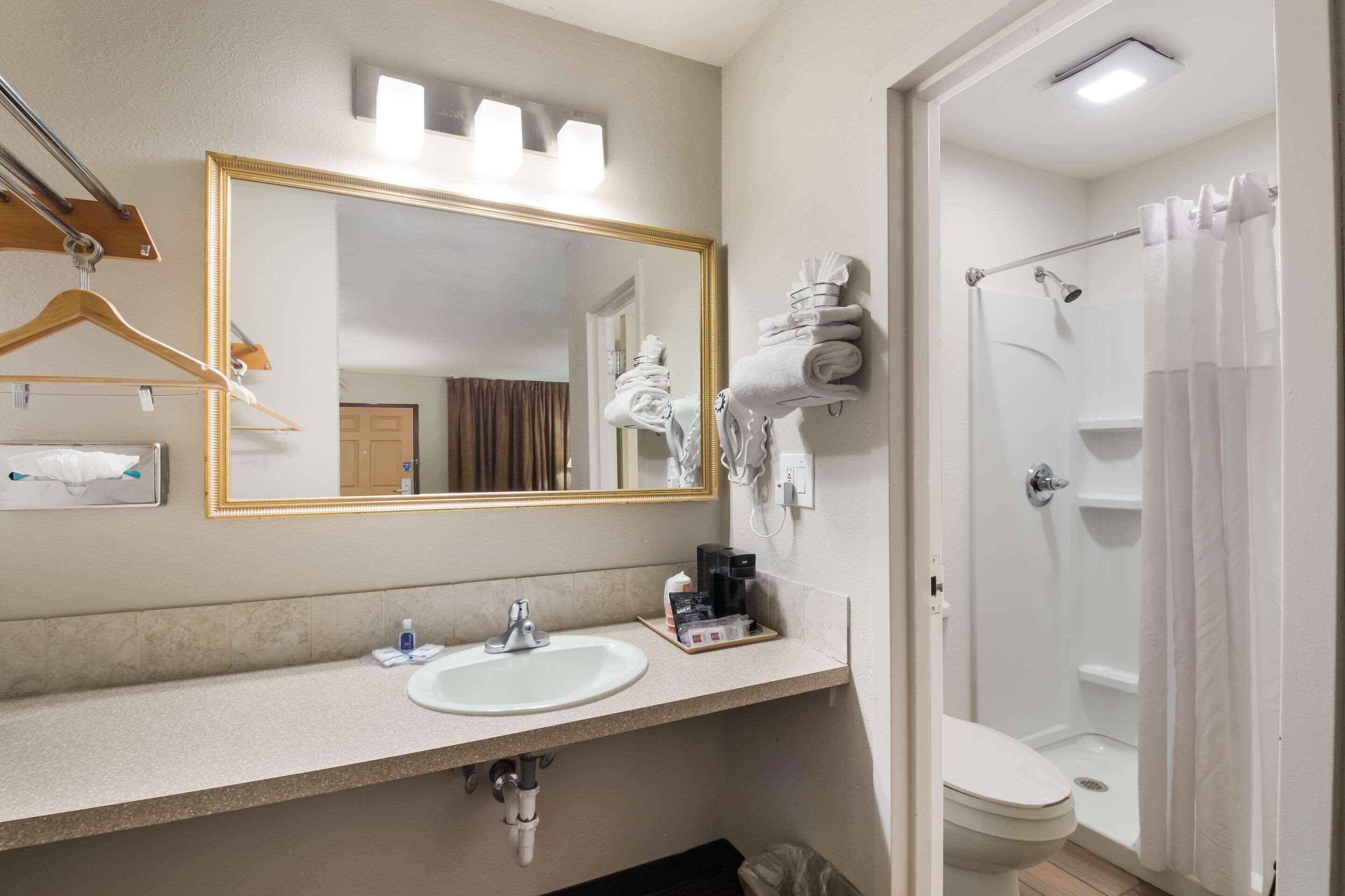 A bathroom with a sink, mirror, towel rack, shower, and toilet.