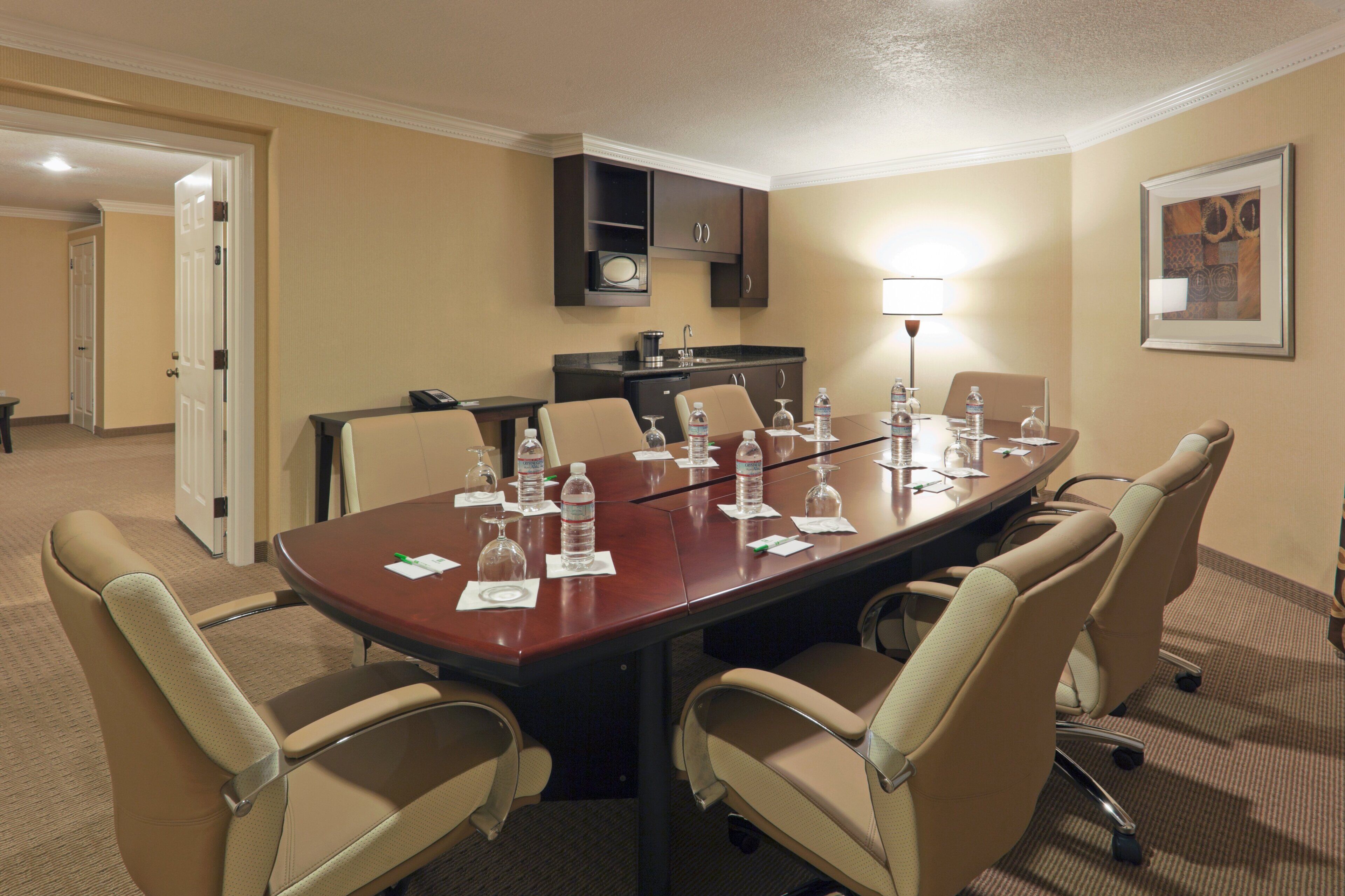 A conference room with a long table, chairs, water bottles, glasses, and a coffee maker.