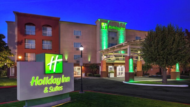 Un bâtiment Holiday Inn & Suites, reconnaissable à son enseigne bien visible, à son entrée abritée et à sa façade bien éclairée.