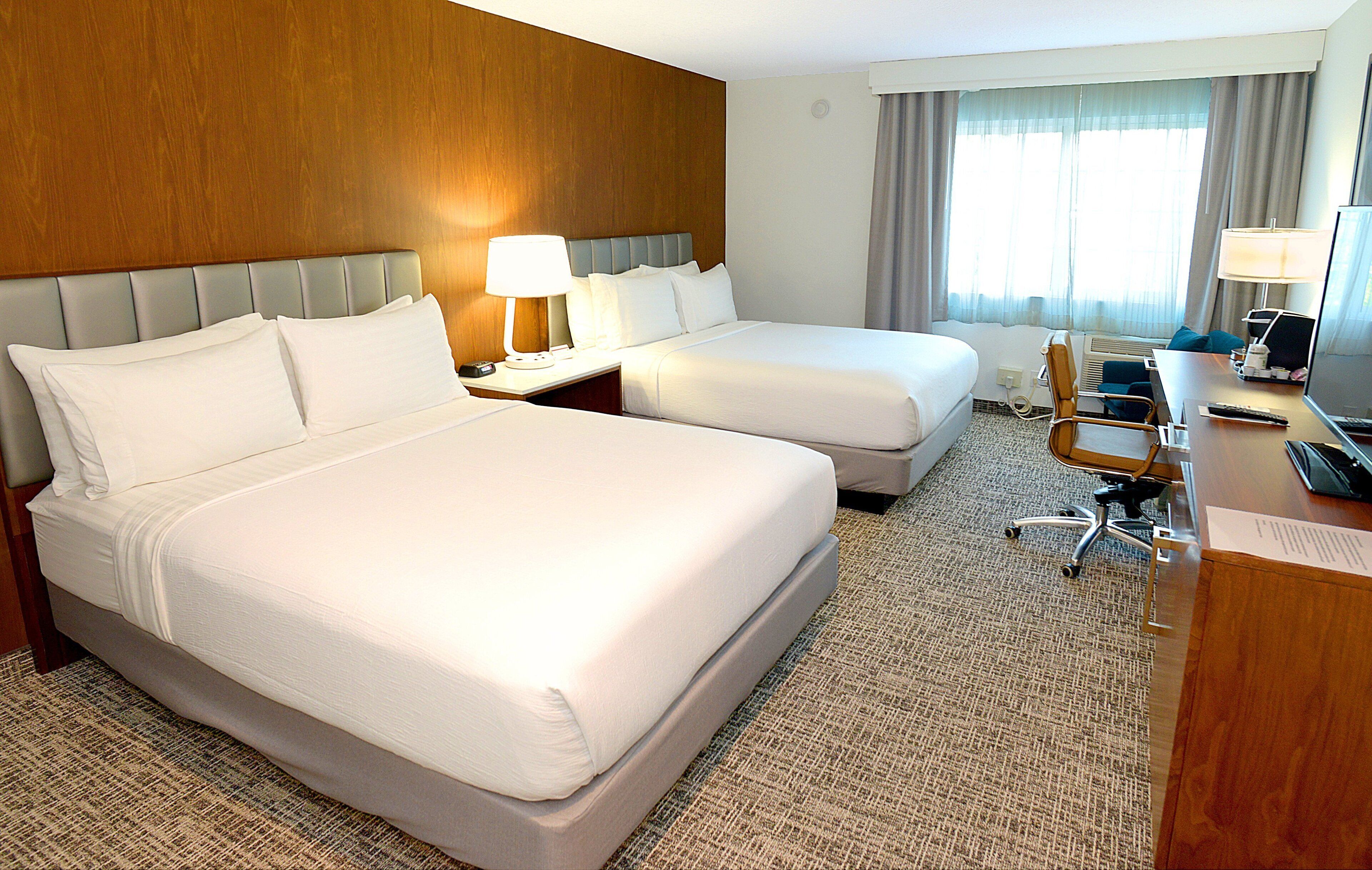 Ein Hotelzimmer mit zwei Betten, einem Schreibtisch mit Computer und einem Stuhl.