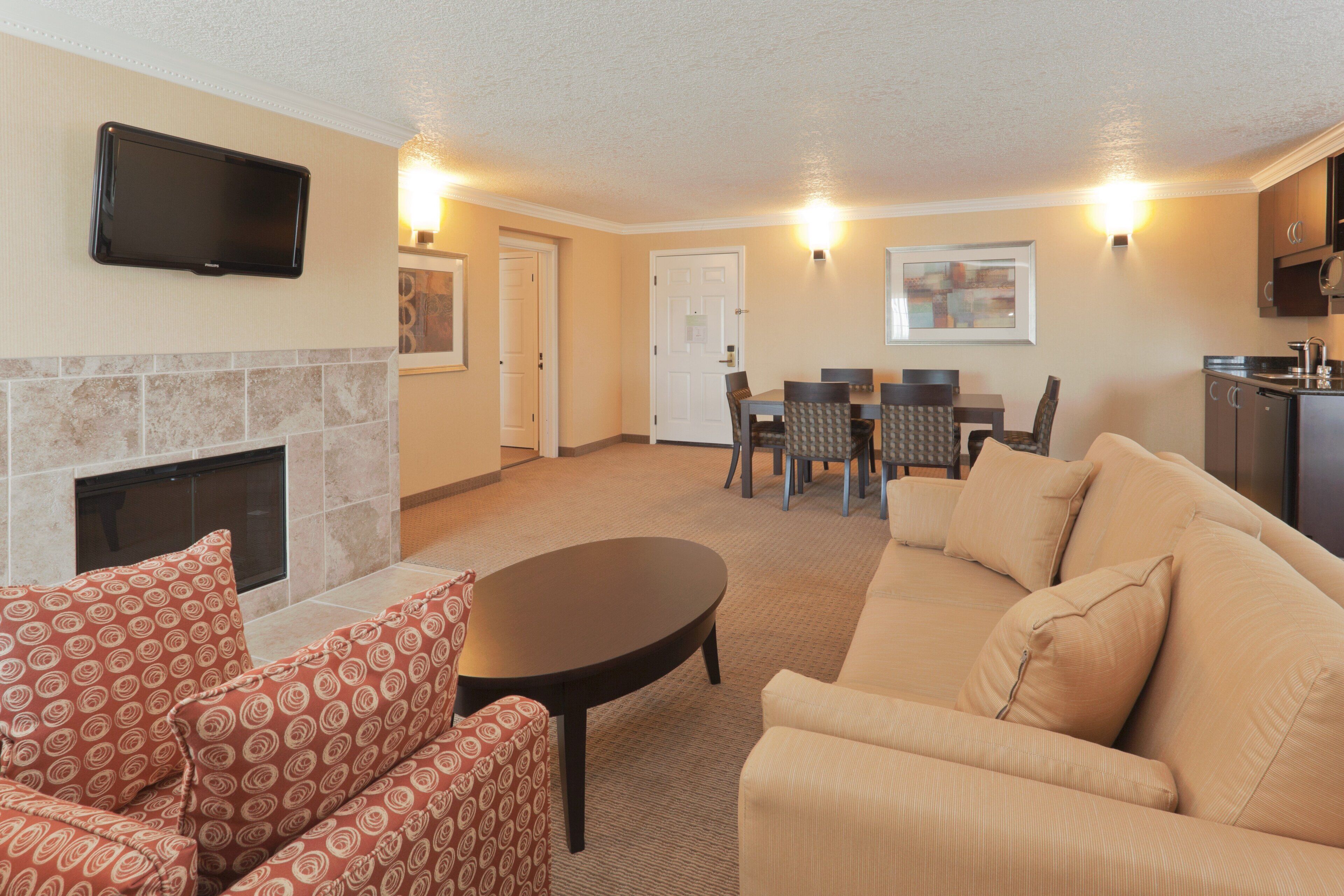 A living room with a fireplace, a sofa, a dining table with chairs, and a flat-screen TV mounted on the wall.