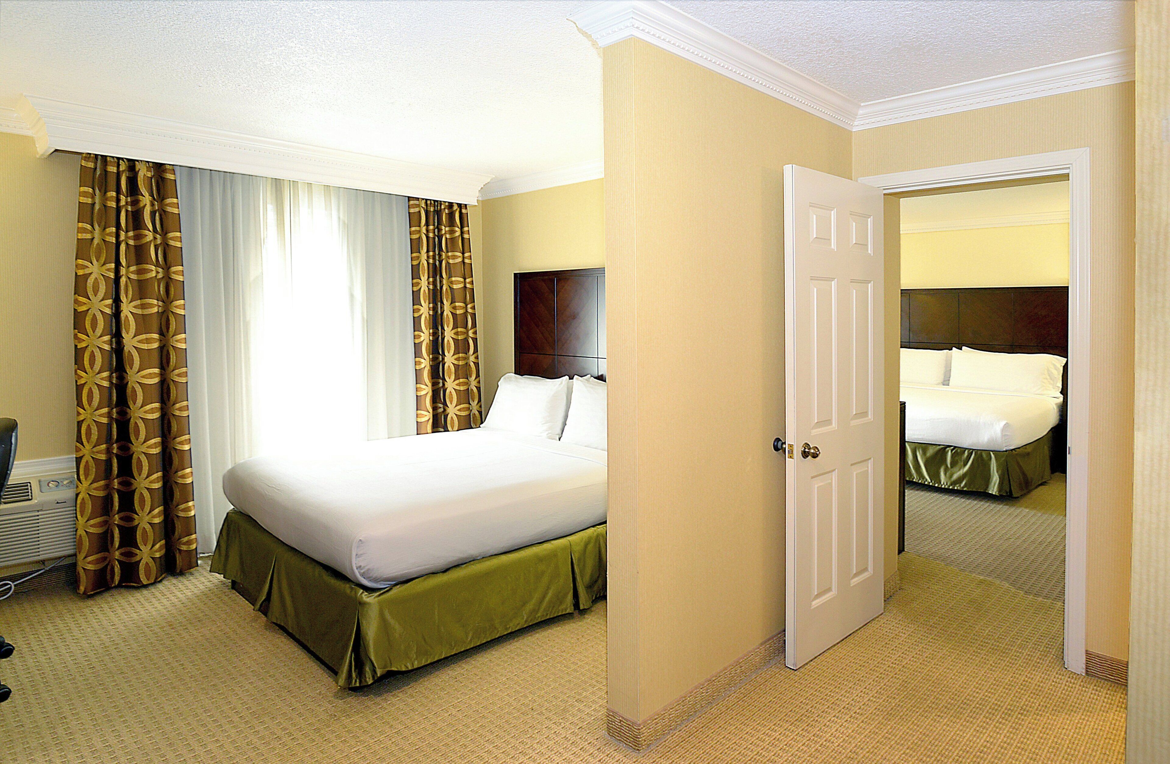 Een hotelkamer met een bed, een deur en uitzicht op een andere kamer.
