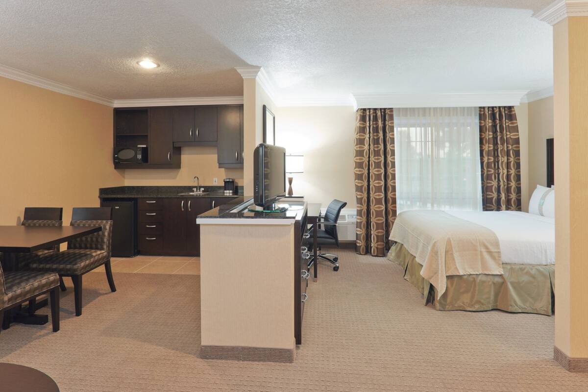 Hotelkamer met een bed, bureau met computer, stoel, een kleine keuken en een raam met gordijnen.
