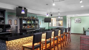 Un espace bar comprenant un comptoir, des tabourets de bar, un téléviseur et une étagère où sont exposées différentes bouteilles.