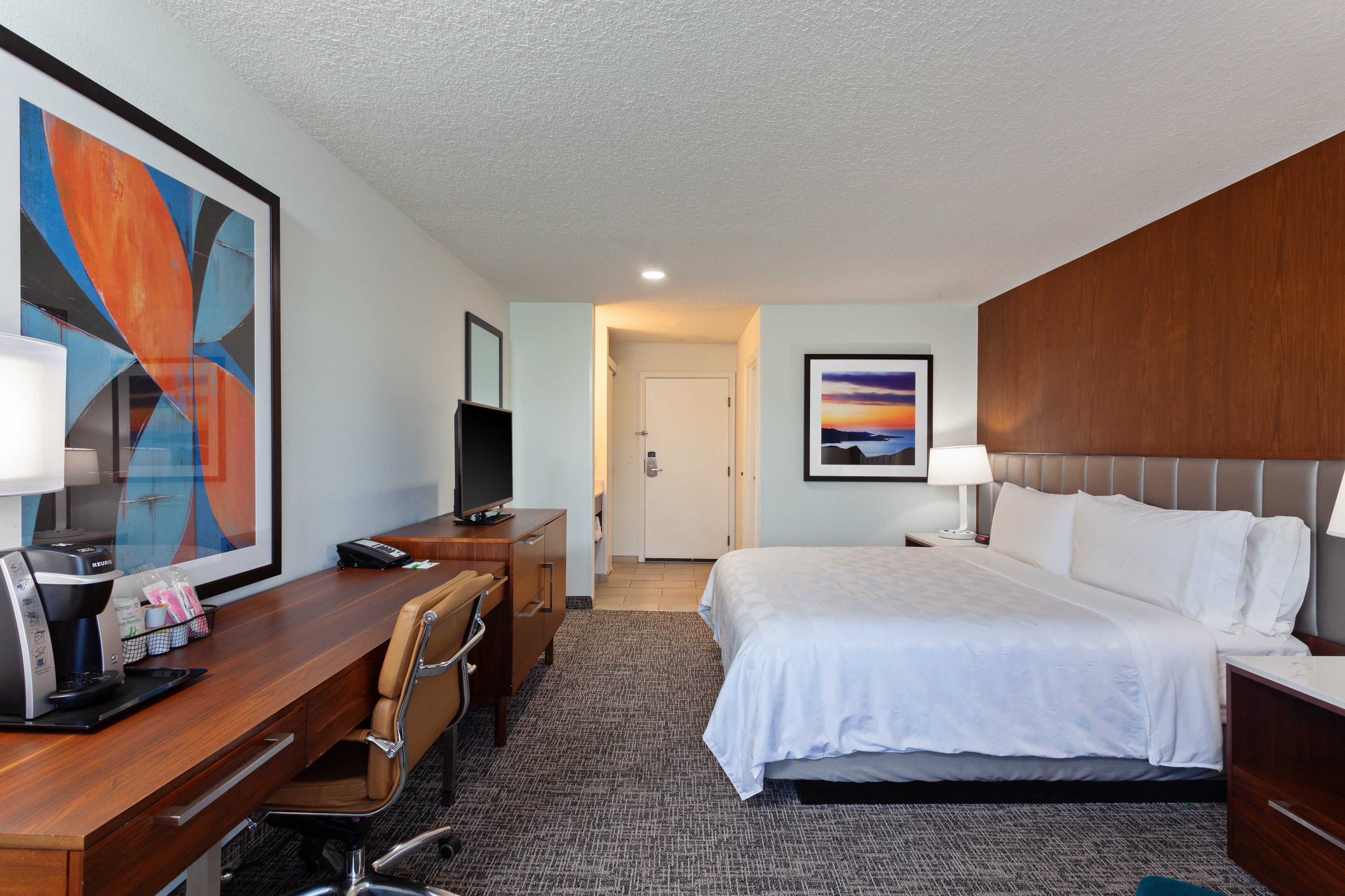 Ein Hotelzimmer mit Bett, Schreibtisch, Stuhl und Bildern an den Wänden.