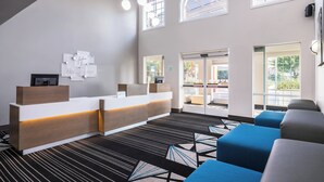 Un espace d’accueil d’hôtel doté d’un comptoir de réception moderne, d’un coin salon et de grandes fenêtres laissant entrer la lumière naturelle.