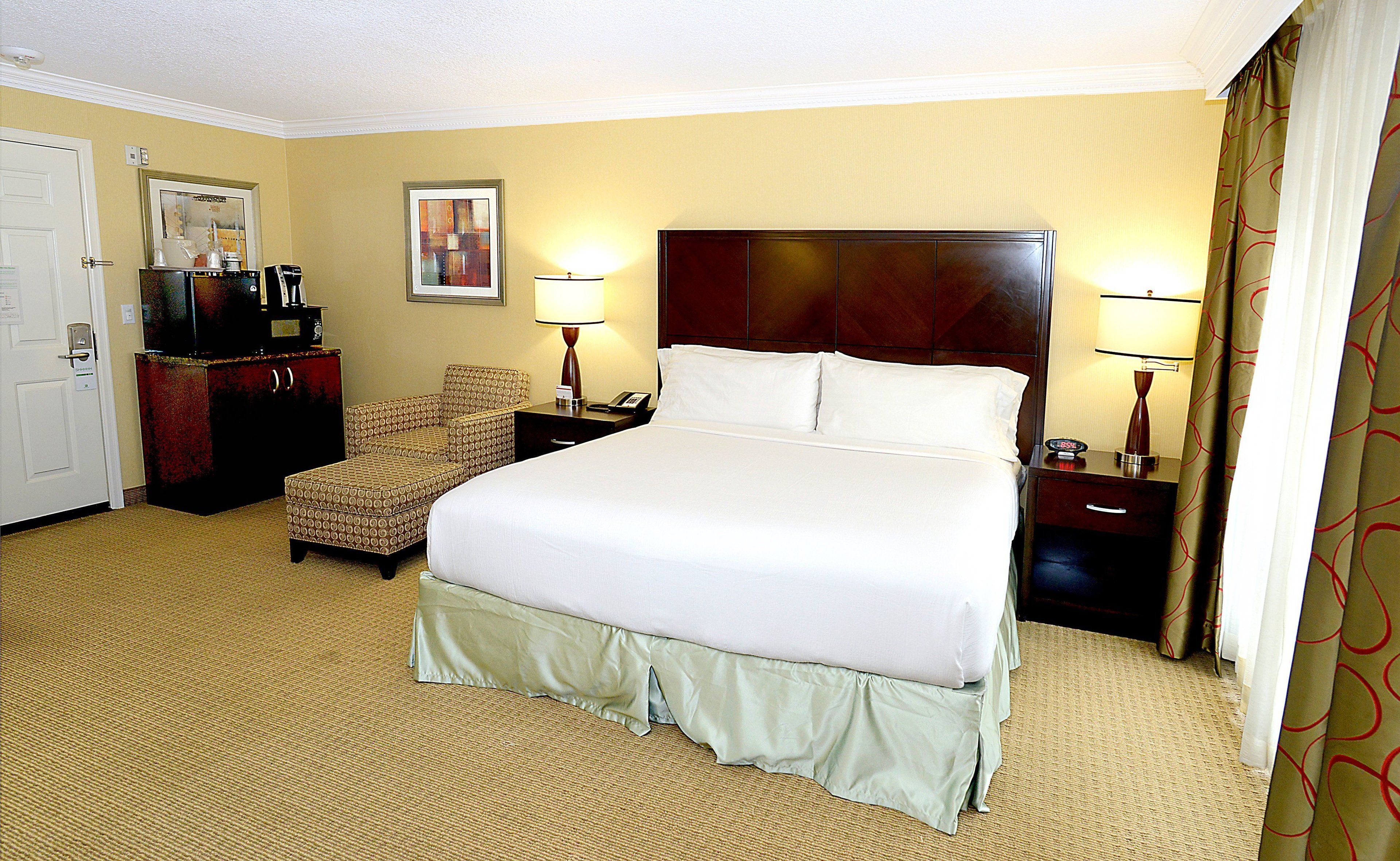 A hotel room with a large bed, a chair, a desk, and a dresser.