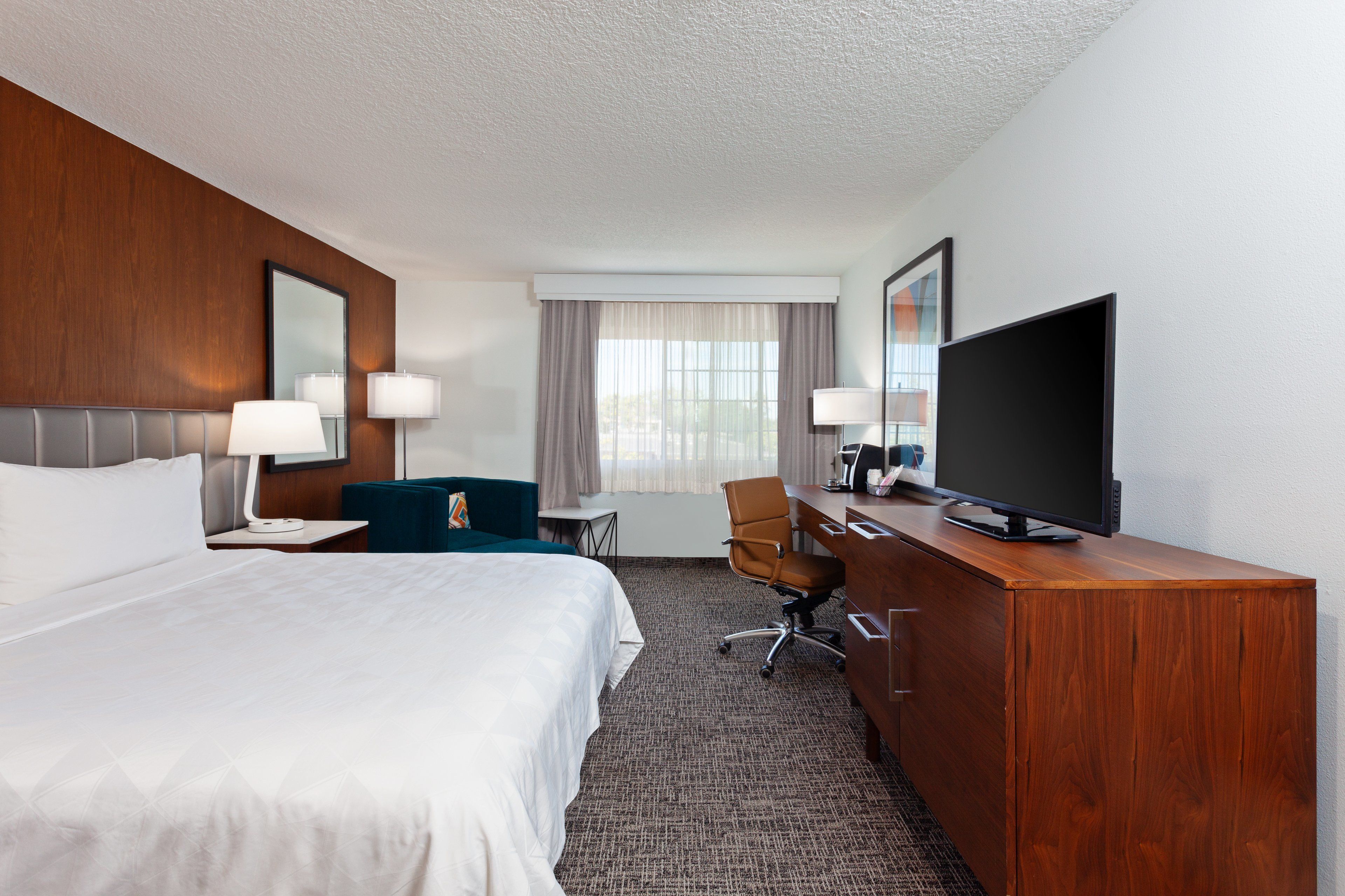 A hotel room with a large bed, a desk, a chair, a television, and a mirror.