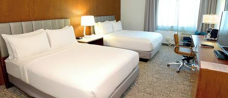 A hotel room with two beds, a desk, a chair, and a television.
