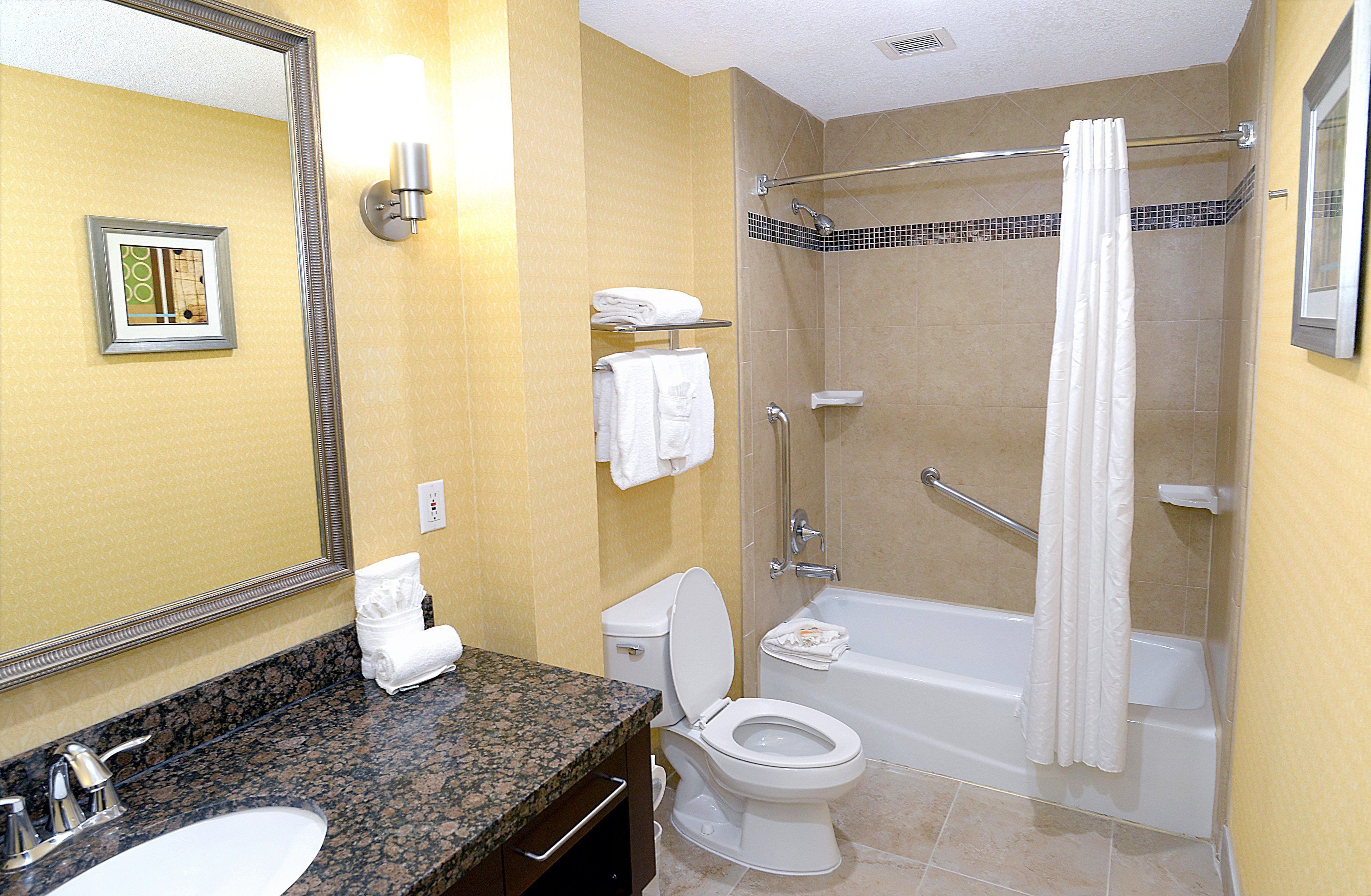 A bathroom with a granite countertop, a white toilet, a bathtub, and a shower with a towel rack.