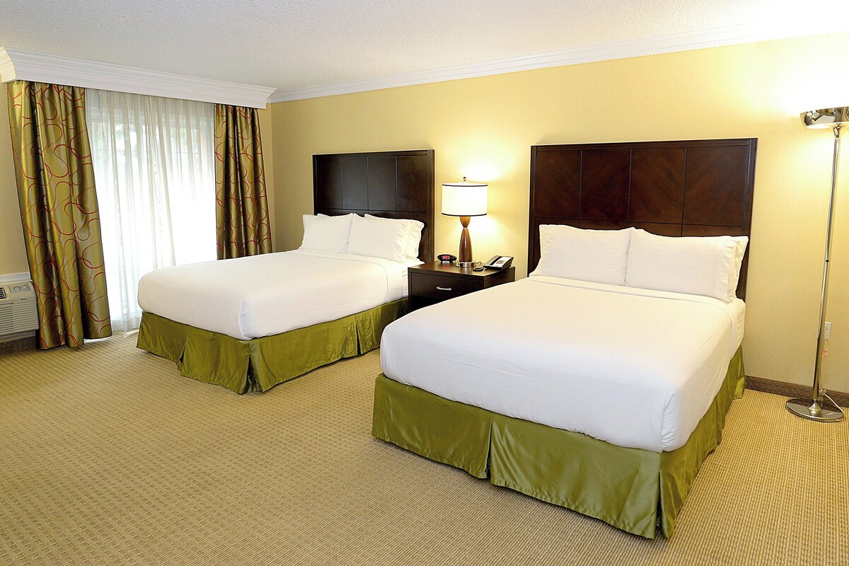 Een hotelkamer met twee bedden, een nachtkastje, een lamp en een raam met gordijnen.