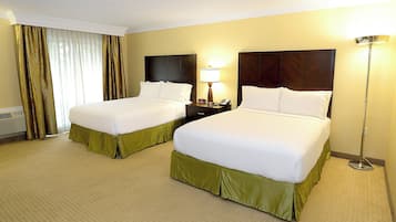 Habitació d'hotel amb dos llits, una tauleta de nit, una làmpada i una finestra amb cortines.