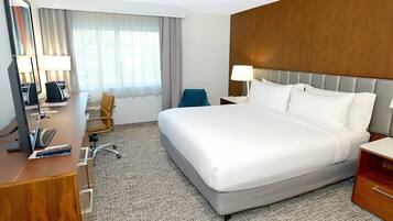 Una habitación de hotel con una cama grande, un escritorio con computadora, una silla, una mesita de noche y un espejo.