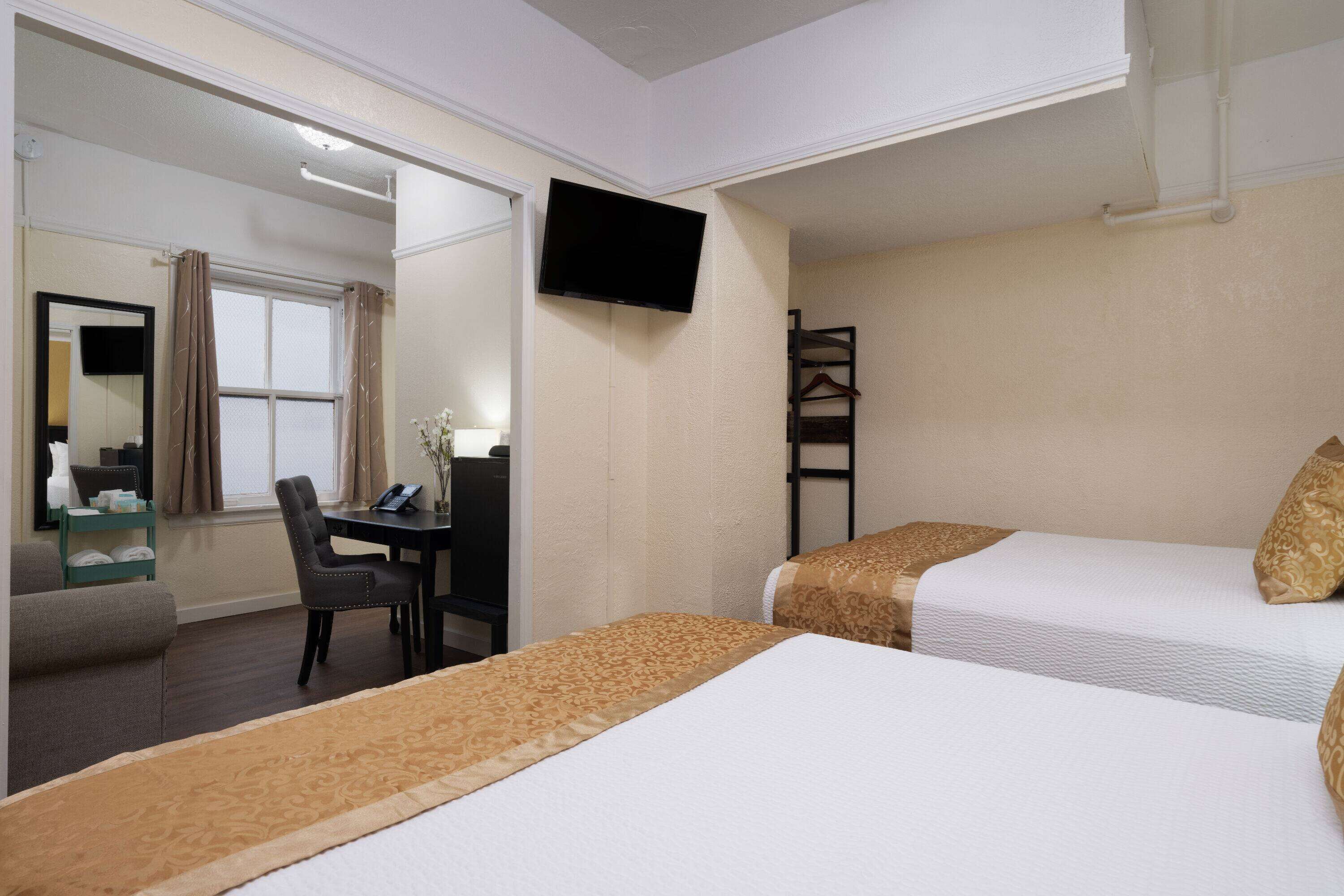 Una habitación de hotel con dos camas, un escritorio, una silla, un televisor y un espejo.
