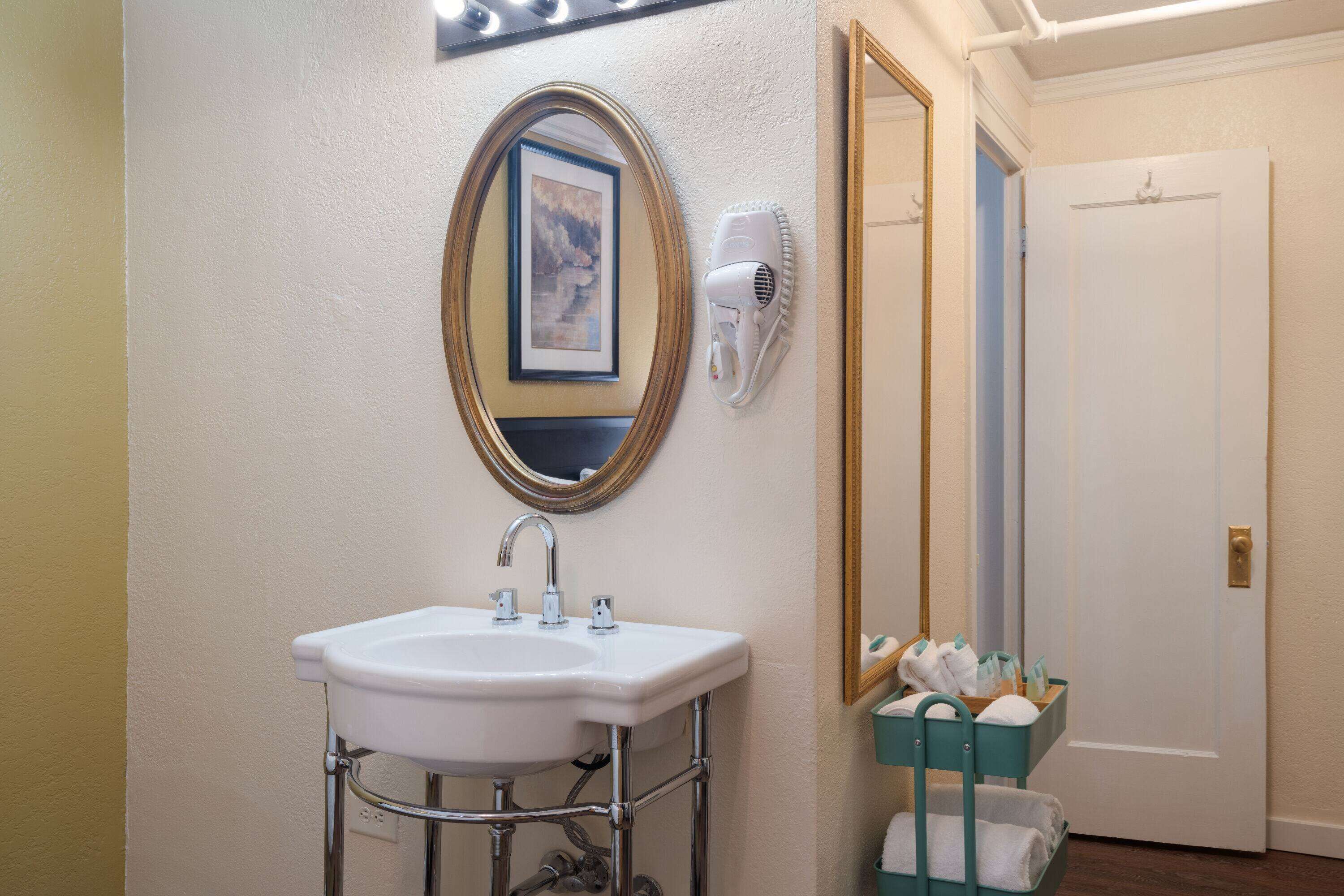 Casa de banho com uma pia branca, um espelho e um secador de cabelo fixado na parede.