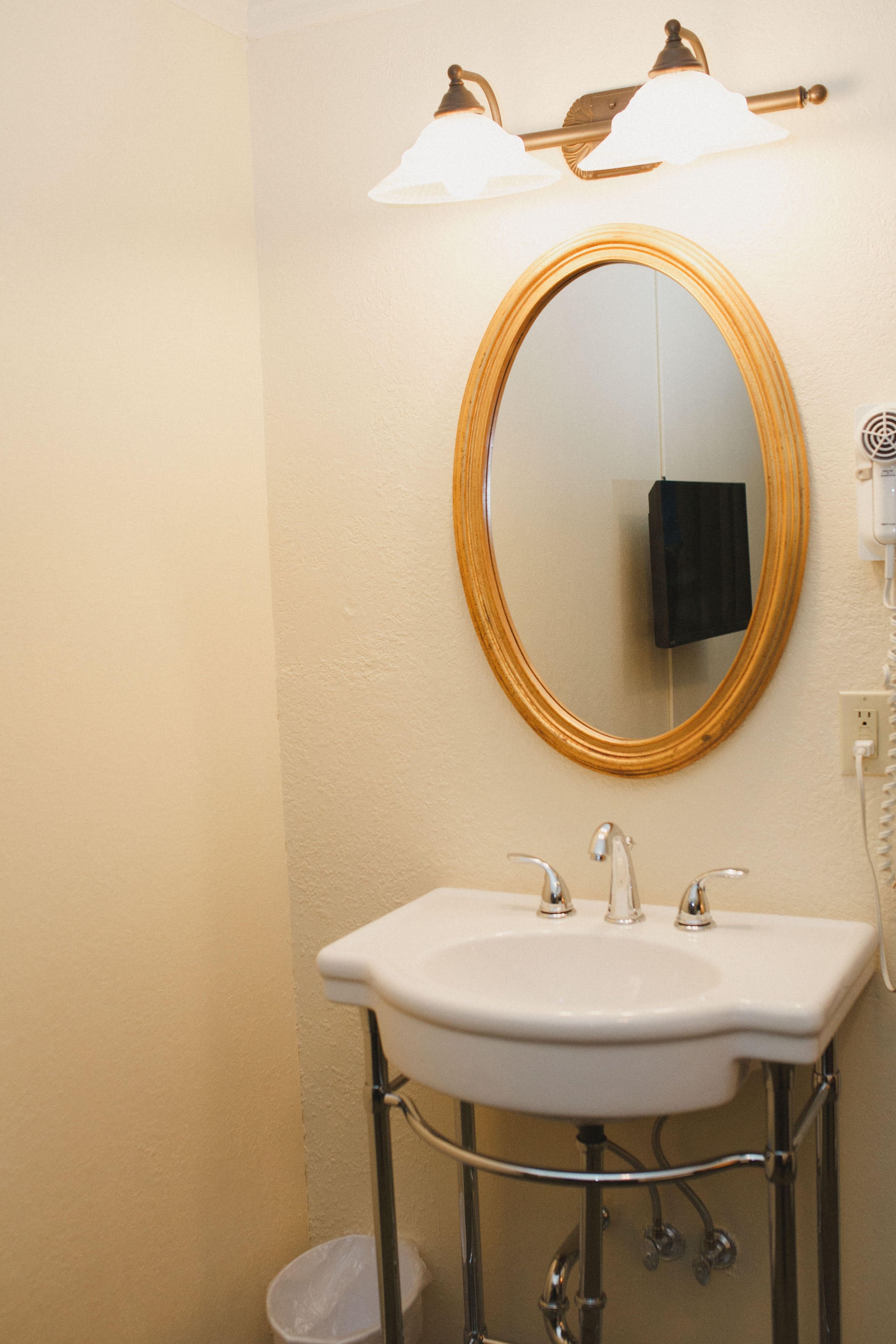 Une salle de bain avec un lavabo blanc, un miroir à cadre doré et une serviette accrochée au mur.