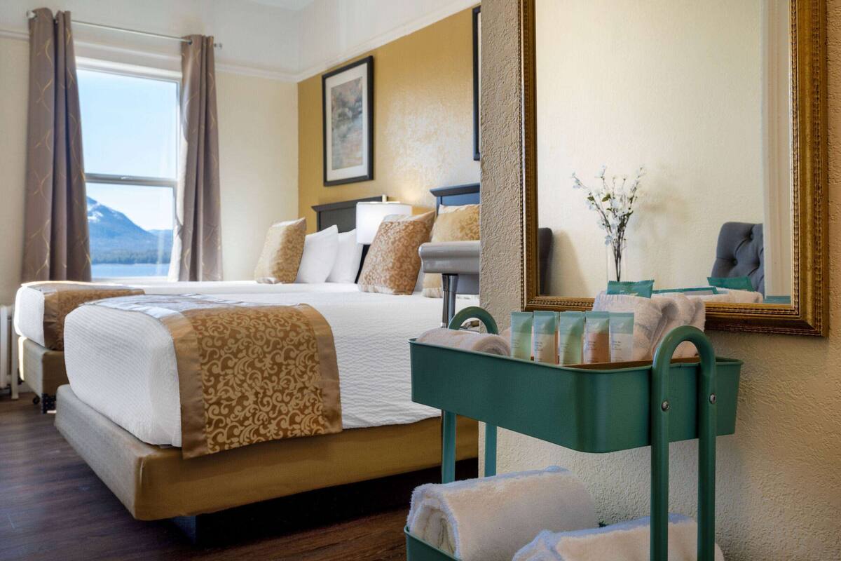 Una habitación de hotel con una cama grande, una mesita auxiliar verde y vistas a las montañas.