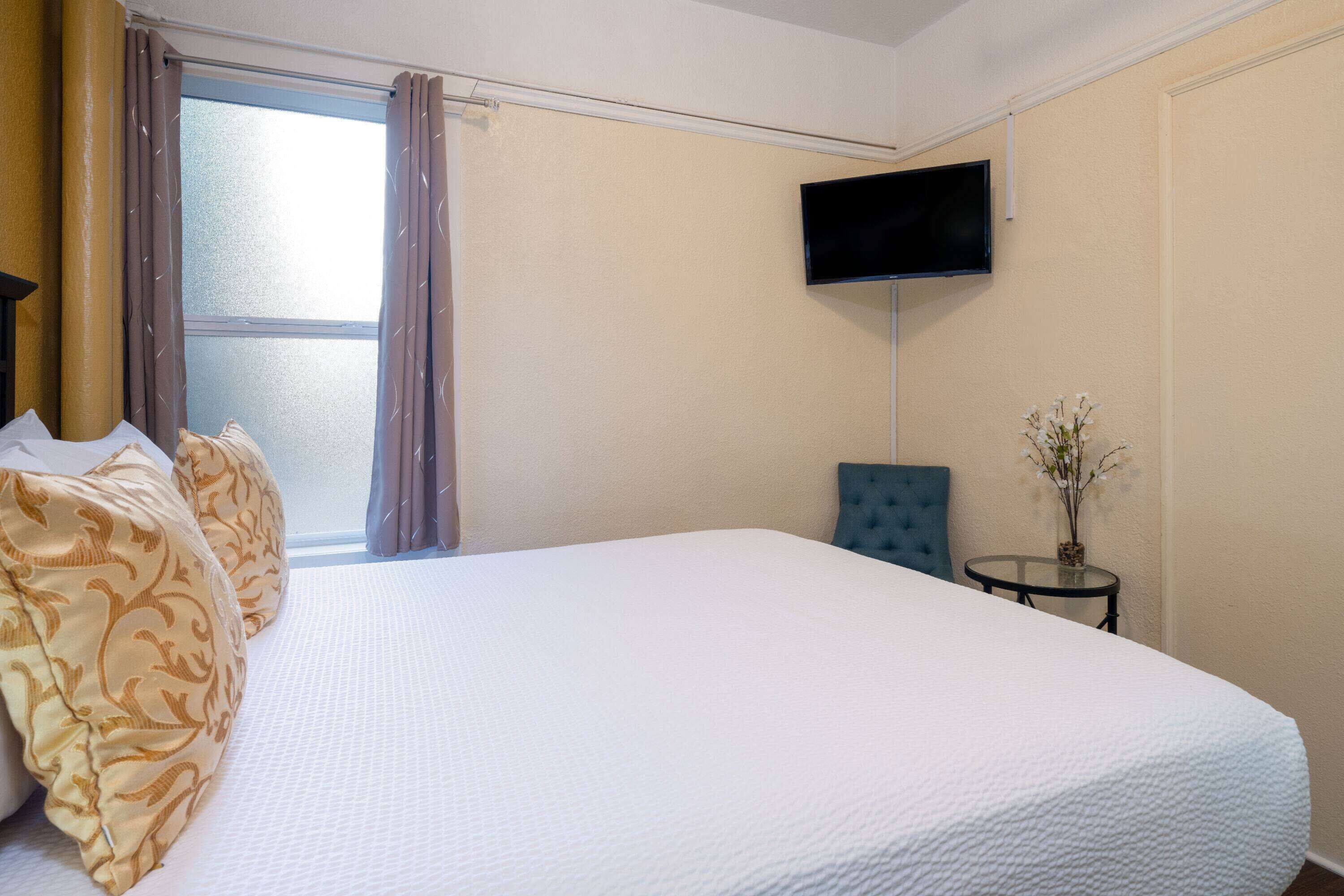 Een hotelkamer met een groot bed, een flatscreen televisie aan de muur, een klein rond tafeltje met een vaas en een raam met gordijnen.