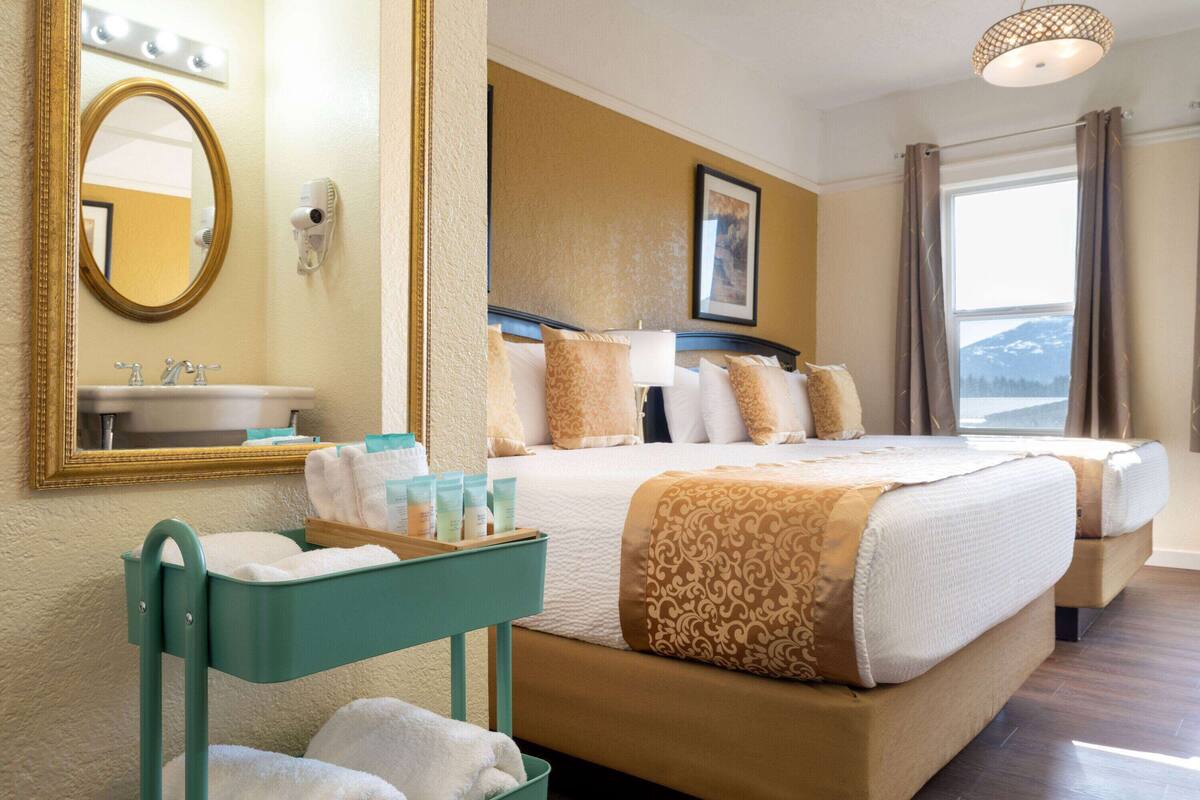 Una habitación de hotel con una cama grande, un baño con lavamanos, un espejo y una ventana con cortinas.