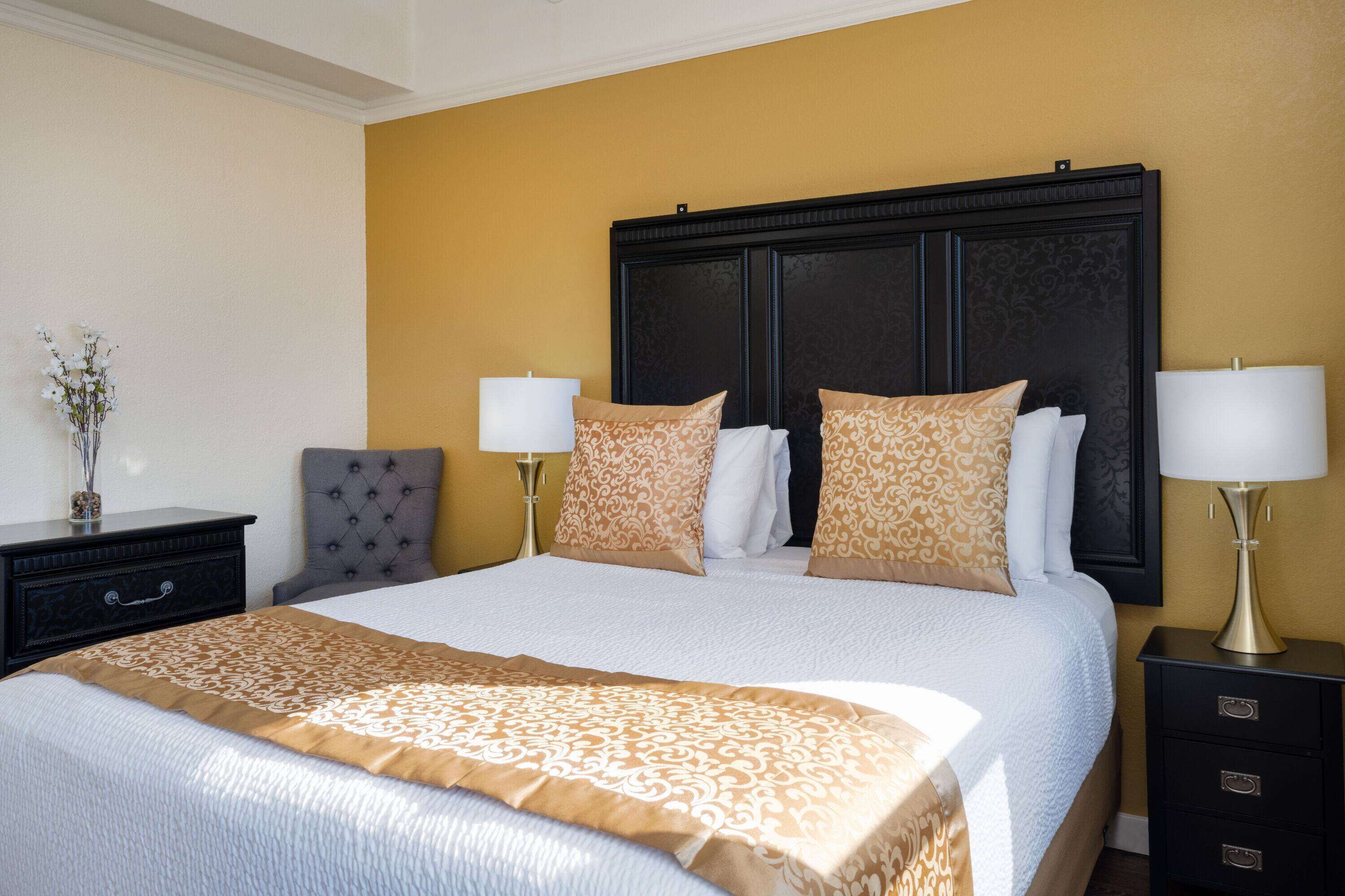 A hotel room with a large bed, two bedside tables with lamps, a chair, and a dresser.