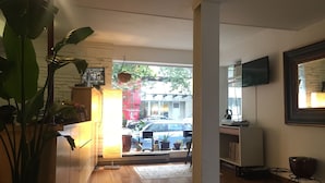 A room with a wooden floor, a large potted plant, a desk with a computer, a television mounted on the wall, and a view of the street outside. - The Dylan, a Baymont by Wyndham (Seattle)