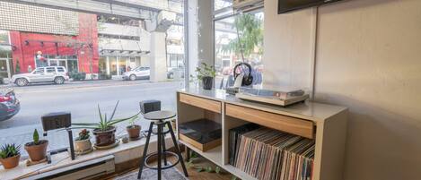 A modern room with a large window, a flat-screen TV, a bookshelf, and a small stool.