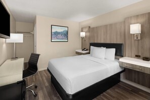 A hotel room with a bed, desk, chair, bedside table, and wall-mounted lamps.