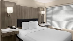 A hotel room with a bed, bedside tables, lamps, a phone, and a window with blinds. - The Dylan, a Baymont by Wyndham (Seattle)