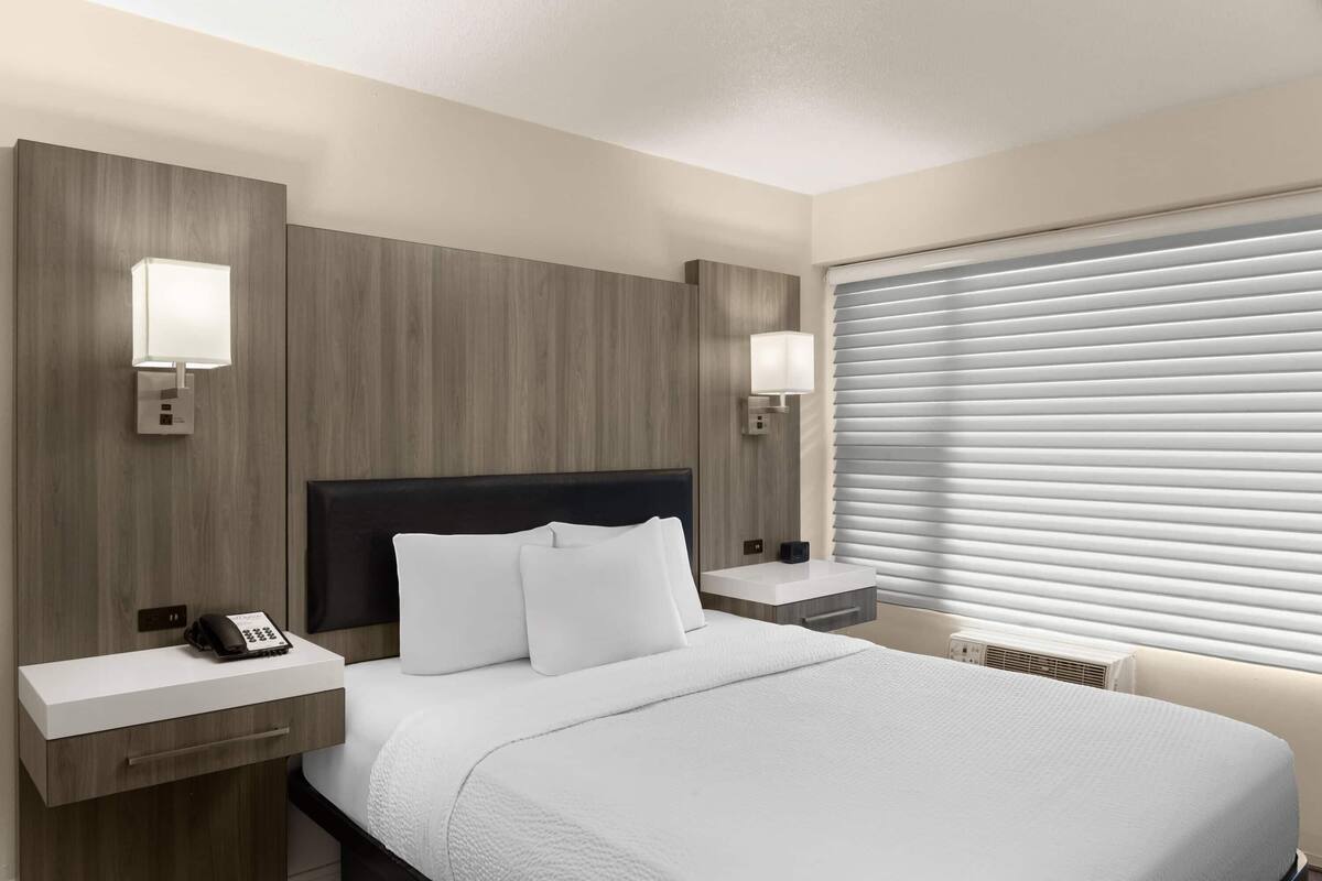 A hotel room with a bed, bedside tables, lamps, a phone, and a window with blinds.